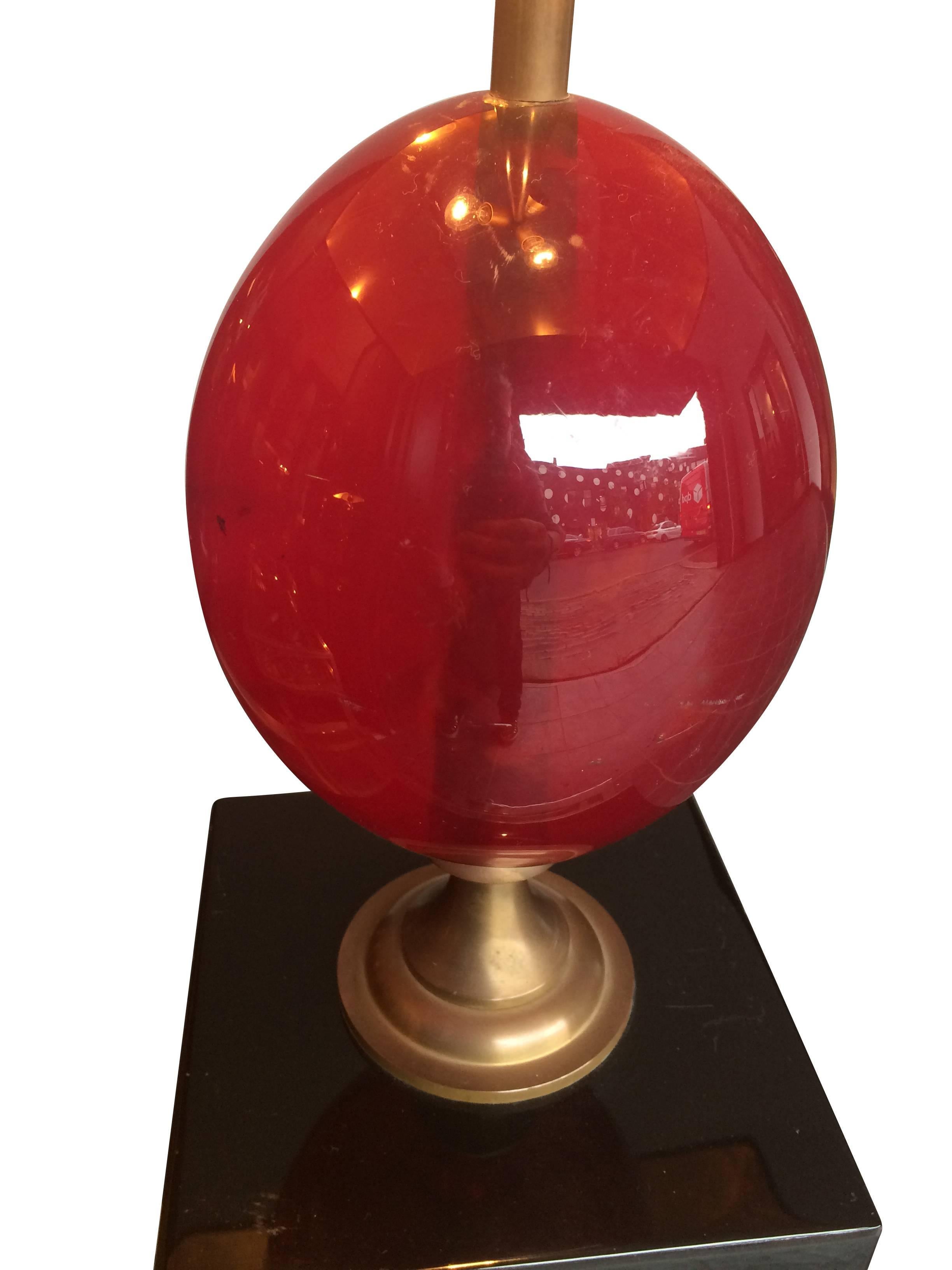 Eine atemberaubende Eierlampe von Maison Charles aus rotem Harz auf einem schwarzen Lacksockel mit abstrakten Details in Gold und Rotgold gesprenkelt. Das große rote Kunstharz-Ei ist auf einem Messingstiel mit Messingbeschlägen montiert. Mit