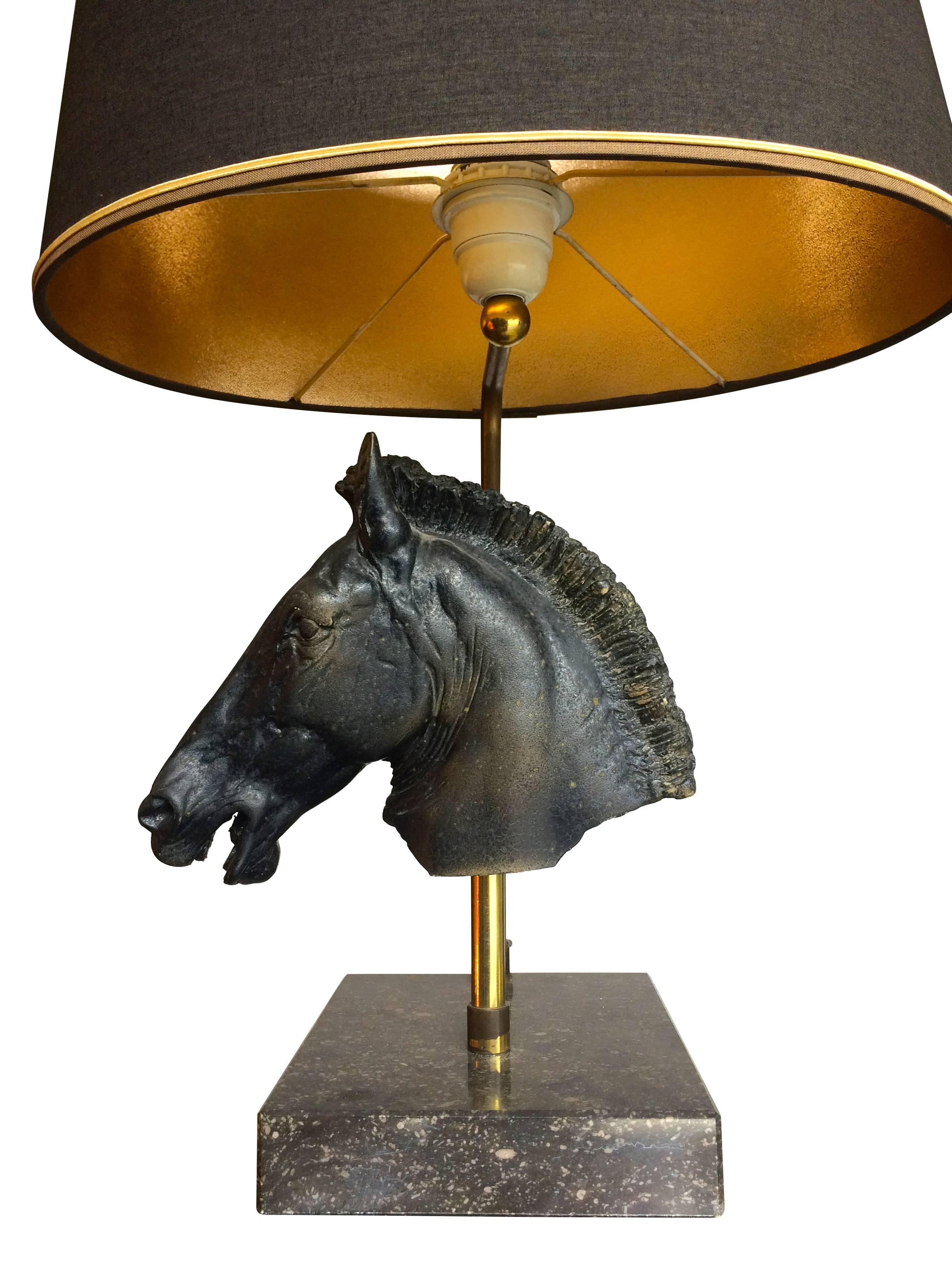 A Maison Jansen style lamp, with black resin sculptural horse head, supported on brass stand on a black marble base, with brass single light fitting supporting an original black shade with gold interior. Re wired with black cord flex and PAT tested.