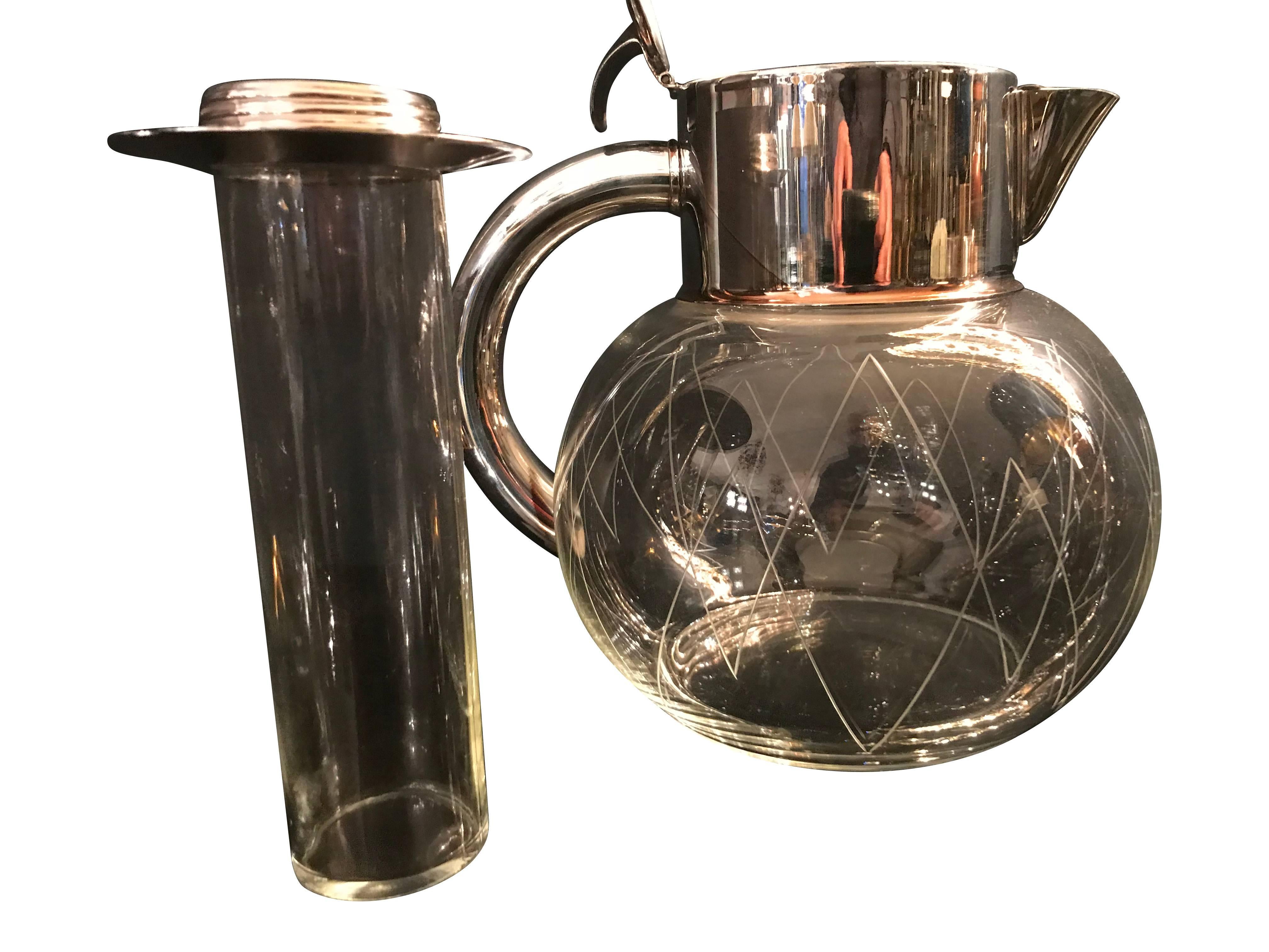 A glass cocktail jug with silver plated handles, lid and strainer. The lid opens to reveal a central glass column to put ice in, which won’t dilute the cocktail or drink in the jug, but keep it iced. The glass bowl is hand cut with geometric lines.