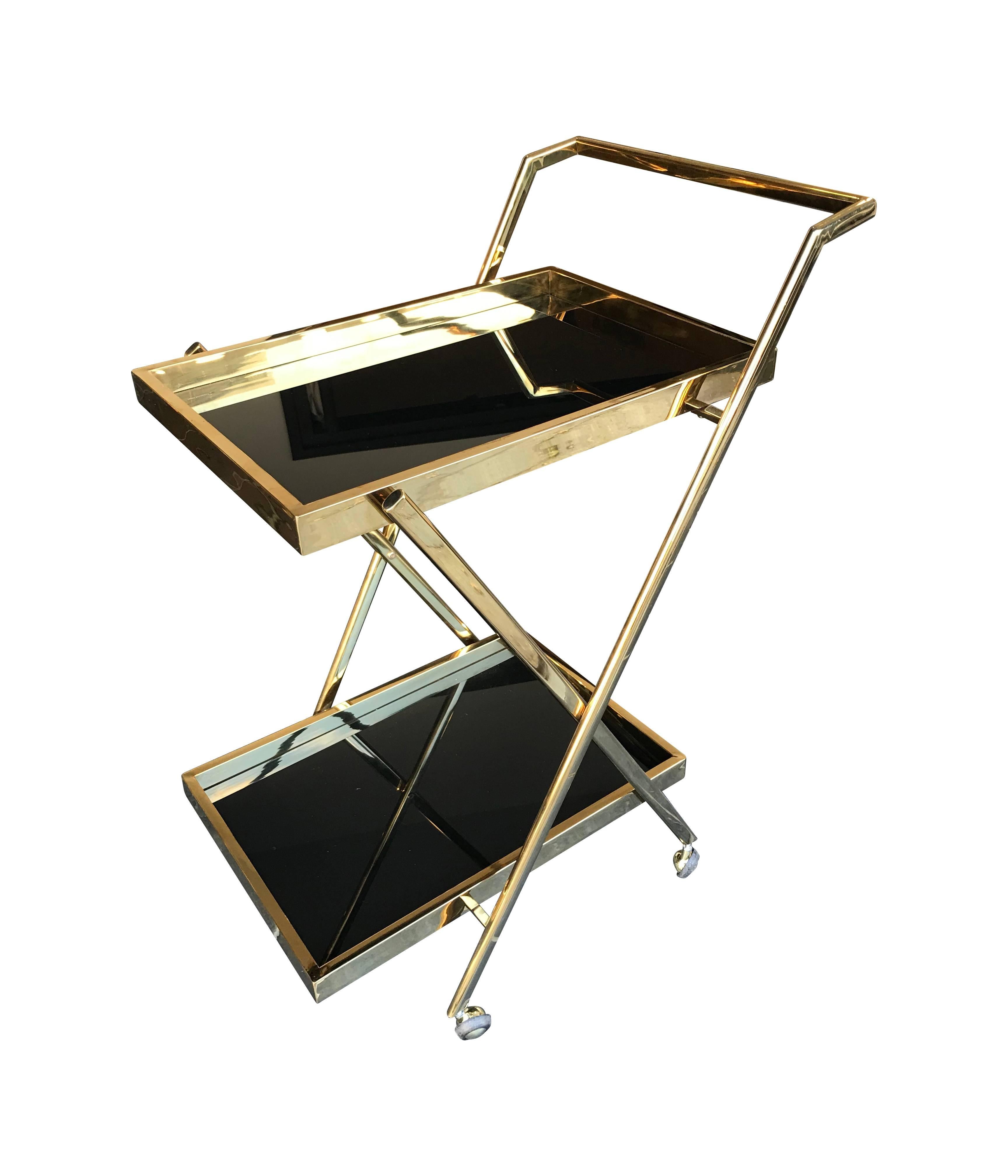 A brass bar trolley with two black glass shelves, raised handle and on castors.