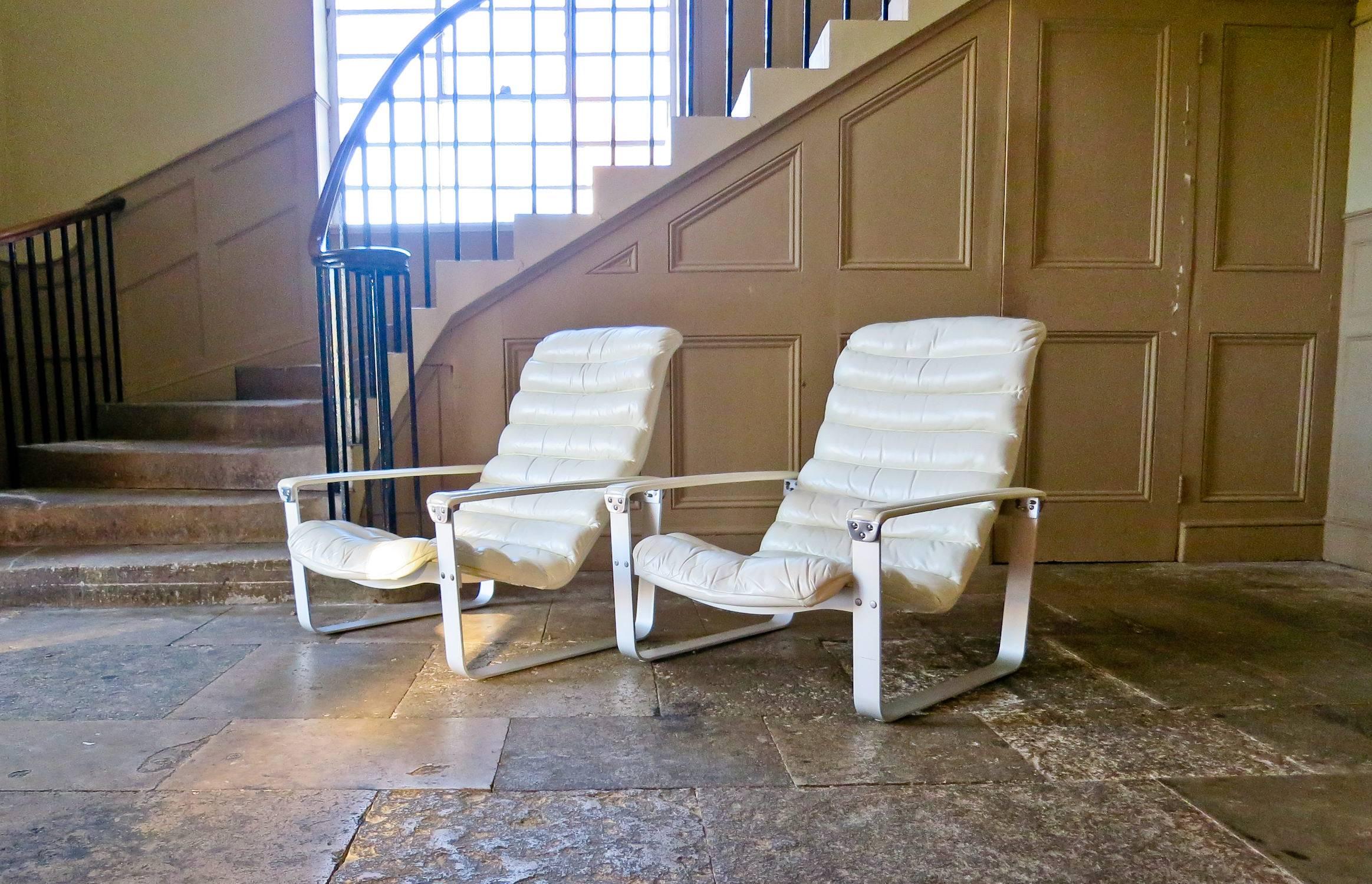 An impressive pair of Pulkka armchairs in cream leather from the 1960s. Padded shaped seat element in leather resting on an brushed aluminium frame with leather armrests held in place by chrome clasps, adjustable for three positions.

The
