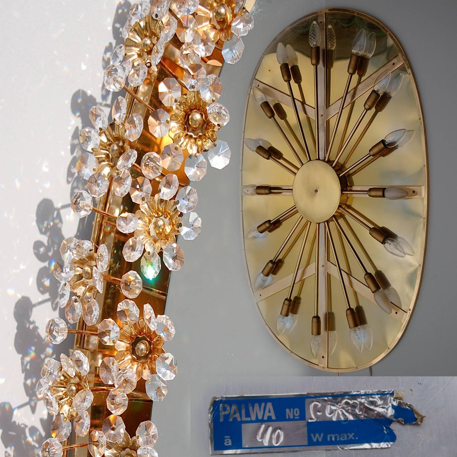 Stunning Mid-Century illuminated oval glass mirror by German manufacturer Palwa. The gilt brass frame is decorated with delicate flowers made from faceted crystals and beads. The center of the flower is finished with a gold-plated detail bolting the