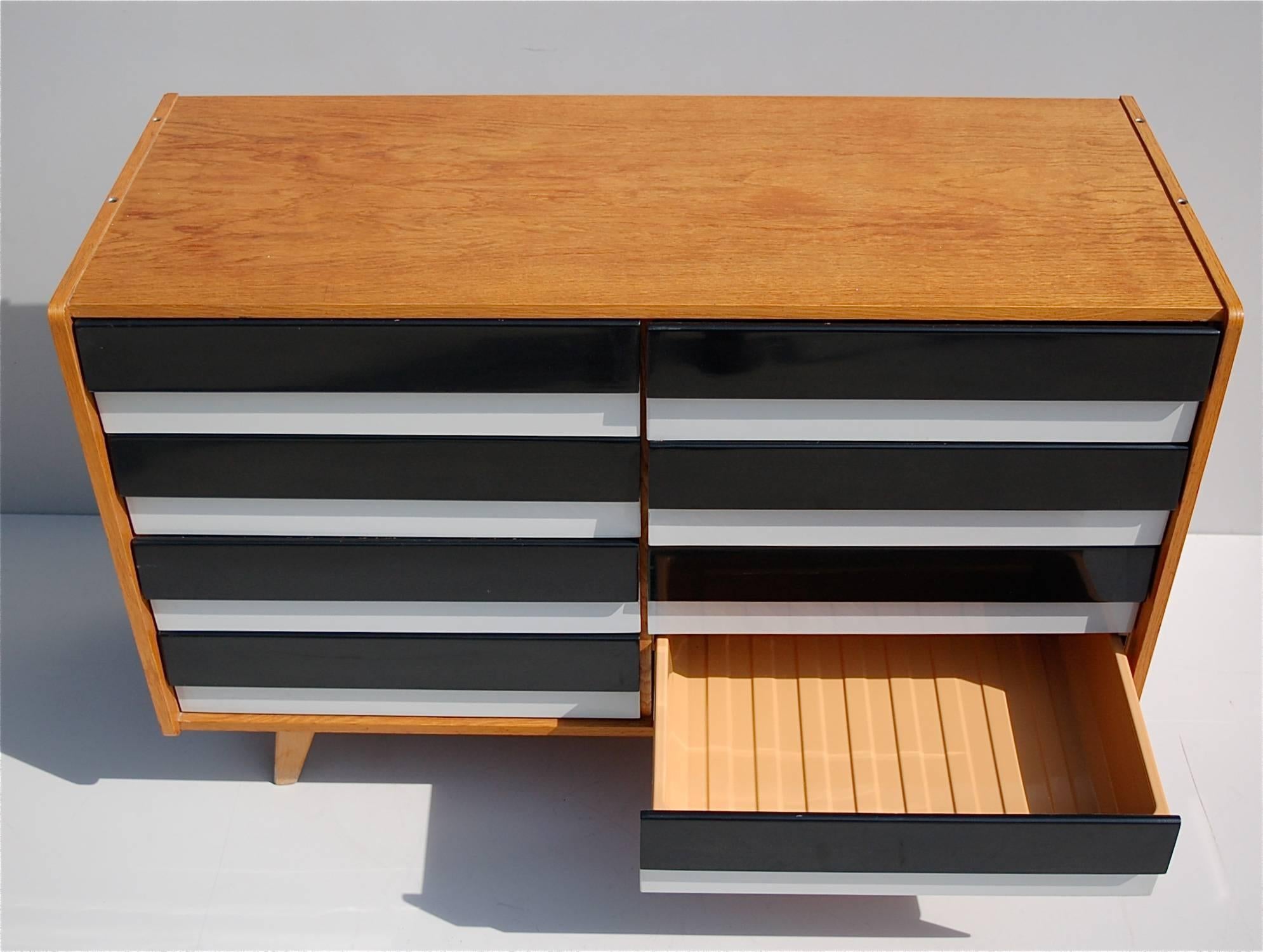A striking chest of drawers with a light wooden frame, designed by Jiri Jiroutek for Interier Praha in the 1960s. The main body is made from solid wood, resting on tapered legs with eight black and white lacquered drawers. Each drawer front has a