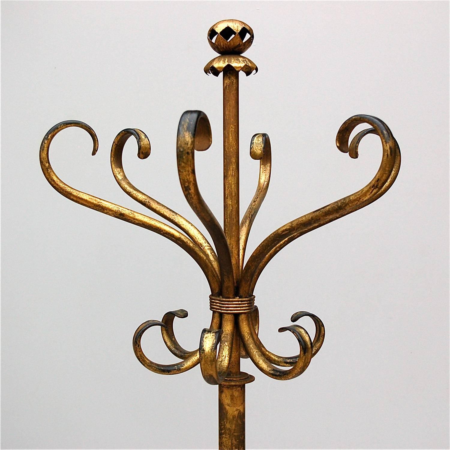 An Italian metal hat and coat stand with antique gold paint finish which has been rubbed in places both through wear and for effect. Six branch crown of double hooks with a decorative finial on a straight column and a wide four leg base.
   