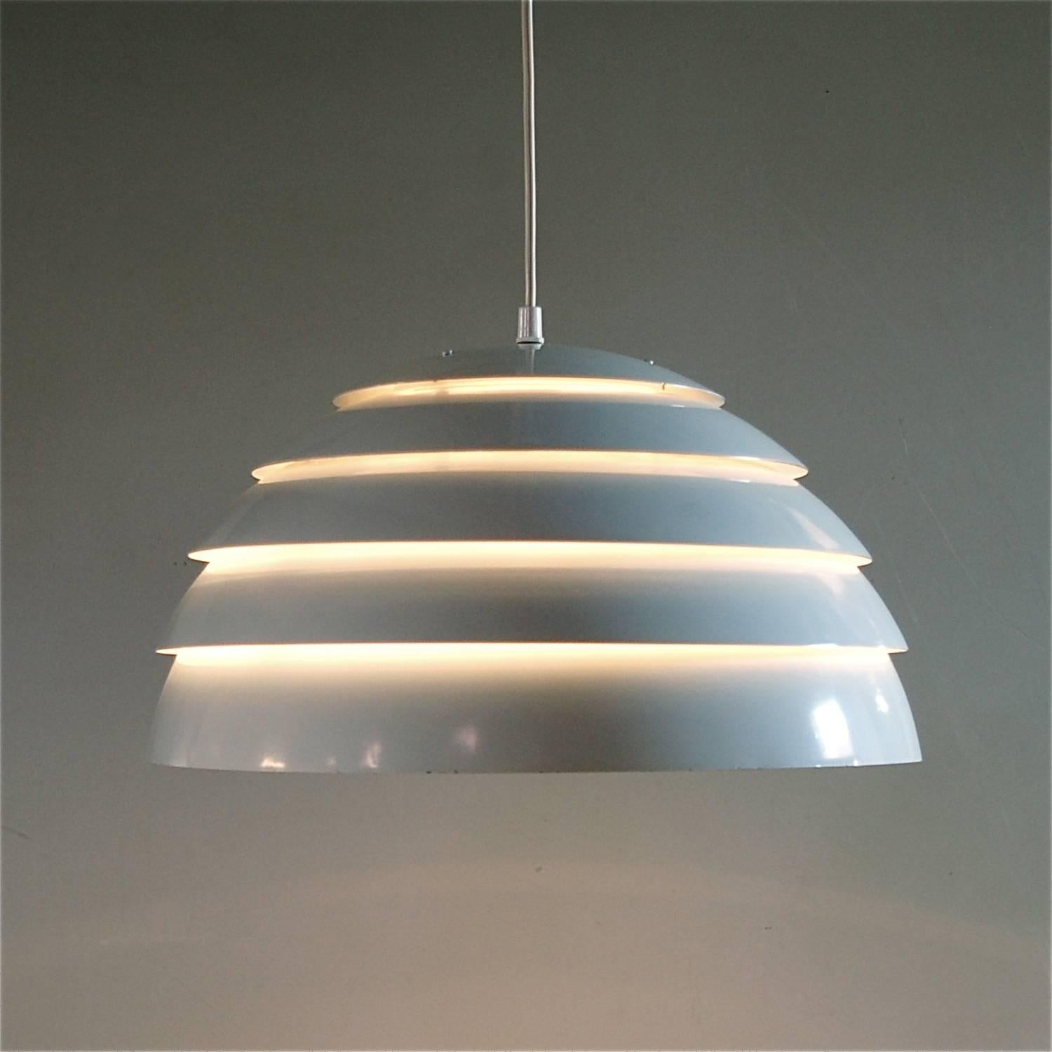 Dome or demilune in shape, this white aluminum pendant, hanging lamp is constructed from overlapping circular layers of powder coated aluminium graduating in seize. The shade also has a white interior and a smaller black inner shade which diffuses