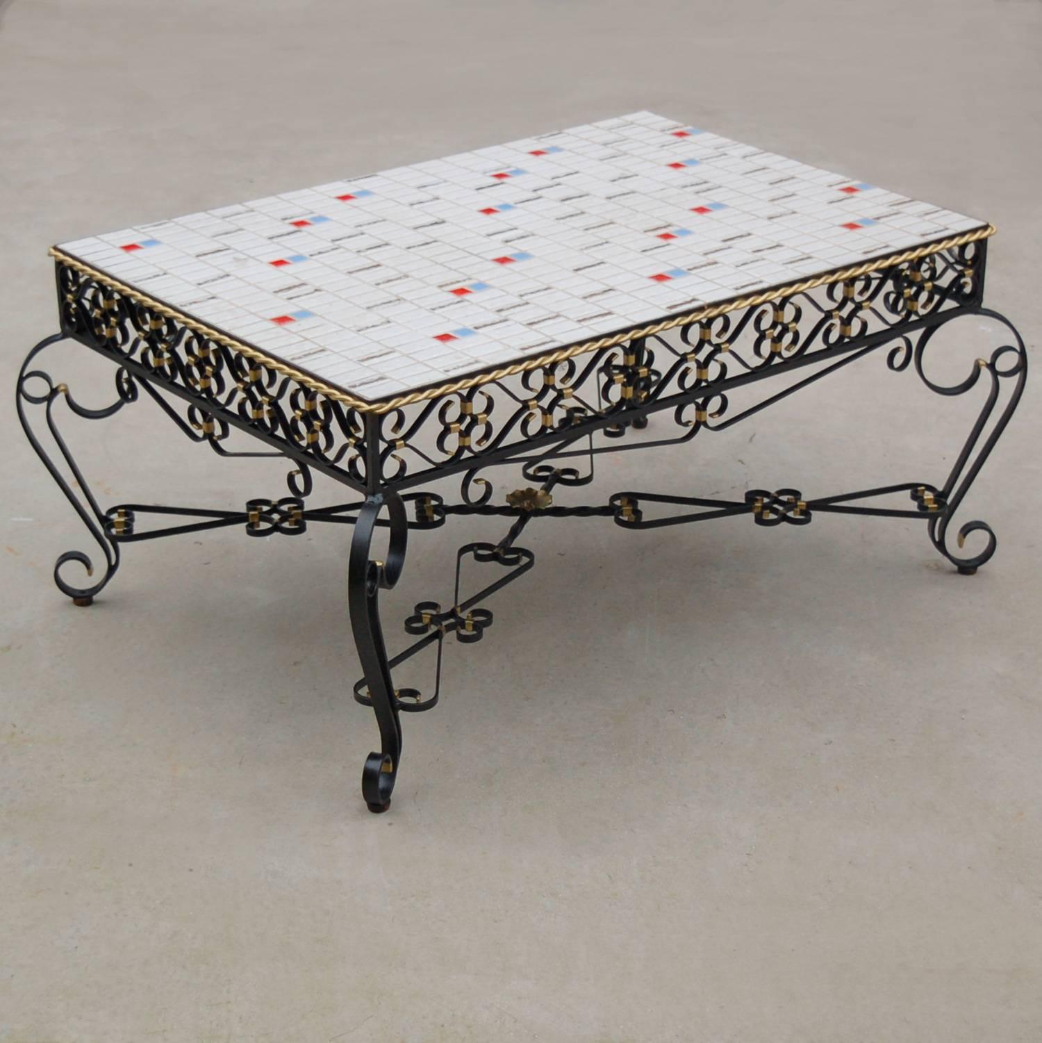 A distinctive rectangular coffee table with mosaic tiled top which rests on a wrought metal frame with elaborate black lacquered scrollwork finished with gold colored highlights and rope edging. The tabletop is decorated with miniature textured