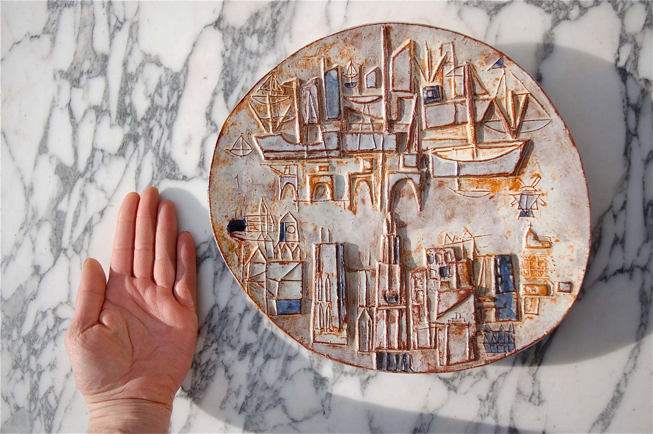 A handcrafted ceramic decorative plate or charger plate with abstract depiction of a harbour cityscape, possibly Rotterdam. The design is raised giving it a wonderful texture and elevating it from a simple decorated plate to a work of art. Because