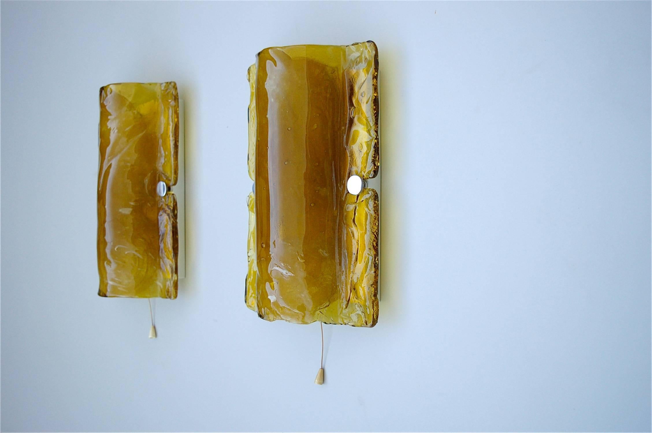 A matching pair of rectangular shaped Murano glass wall sconces or wall lights. They are flush mounted and have a curved shape in the centre. The thick glass is a deep cadmium, almost ochre yellow which comes alive when the sconces are lit. They