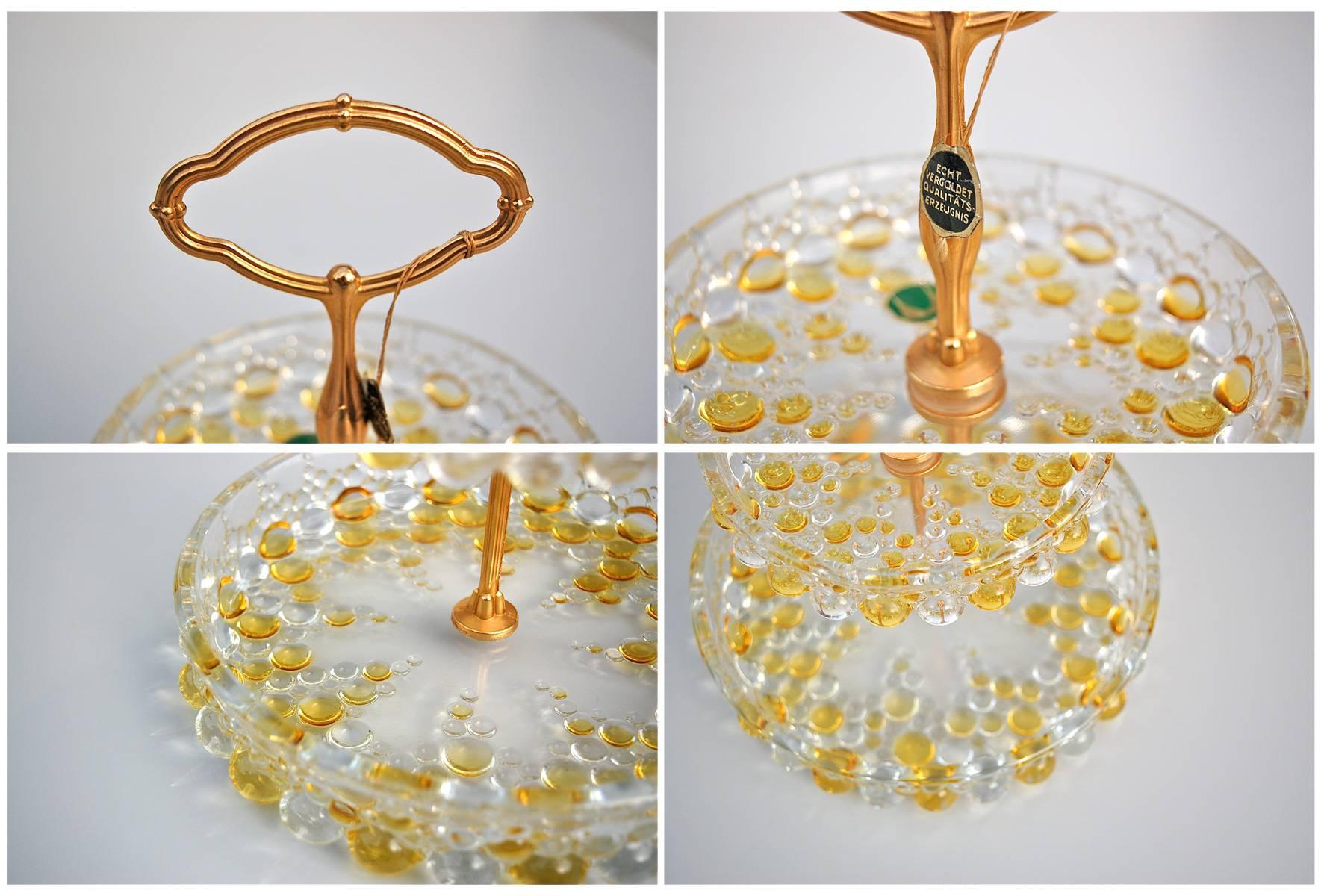 This two-tiered circular stand is made from glass with clusters of bubbles in clear and yellow glass. The bottom tier appears to be floating on the larger bubbles around the base and the pattern is repeated on the second, smaller tier. The stand has