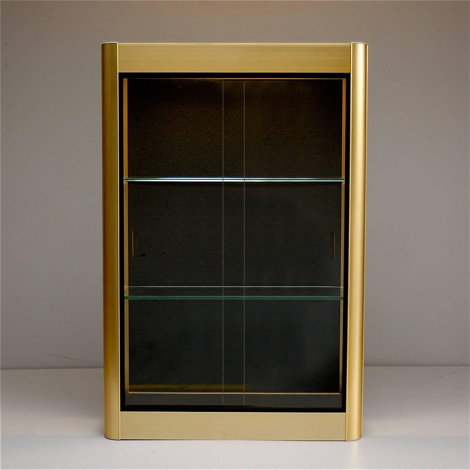 Gold colored aluminium display cabinet with sliding glass doors and round edges. It has built in tube light which helps create a great backdrop for displaying any collectibles or jewelry. It could also function as an apothecary or bathroom cabinet.