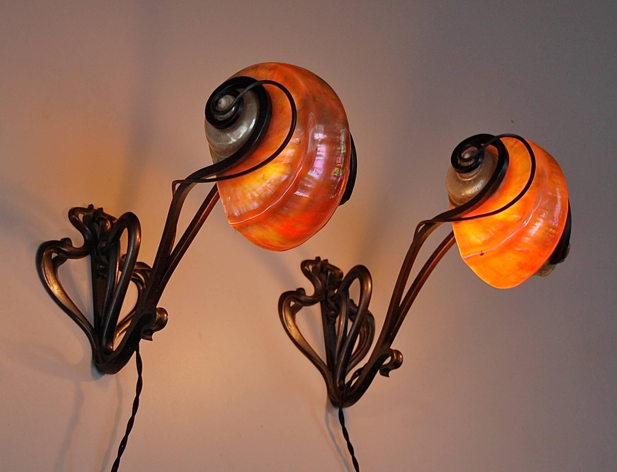 A pair of Nautilus lamps with bronze patinated feet which support the shell diffuser. The style is quintessentially Art Nouveau. The design of the base is a joining together of long sinuous lines that weave themselves like branches around the outer
