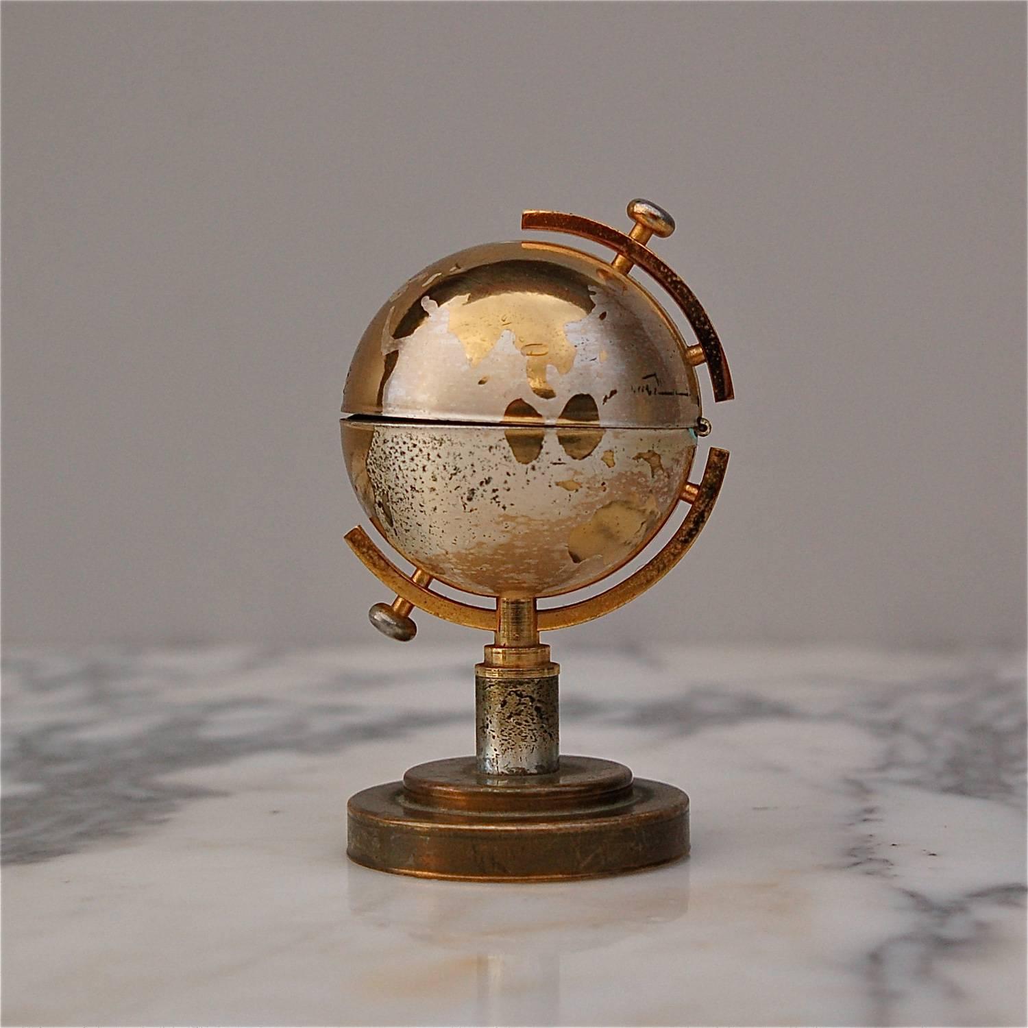 At first sight, you'd never imagine this shiny little globe would morph into a cigarette lighter. By a simple pull, the top hemisphere flips open revealing the inner part with striker. This lovely decorative item is very evocative of the glamorous
