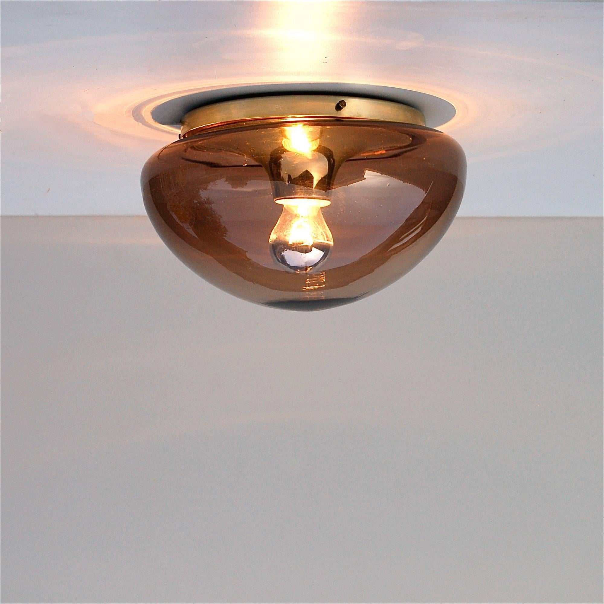 This 1970s flush mounted RAAK style lamp can be used as either a ceiling or wall light. It has a large dome shade in smoked glass with a single light source at the centre of the aluminium base. The light requires a single E27 lightbulb and is in