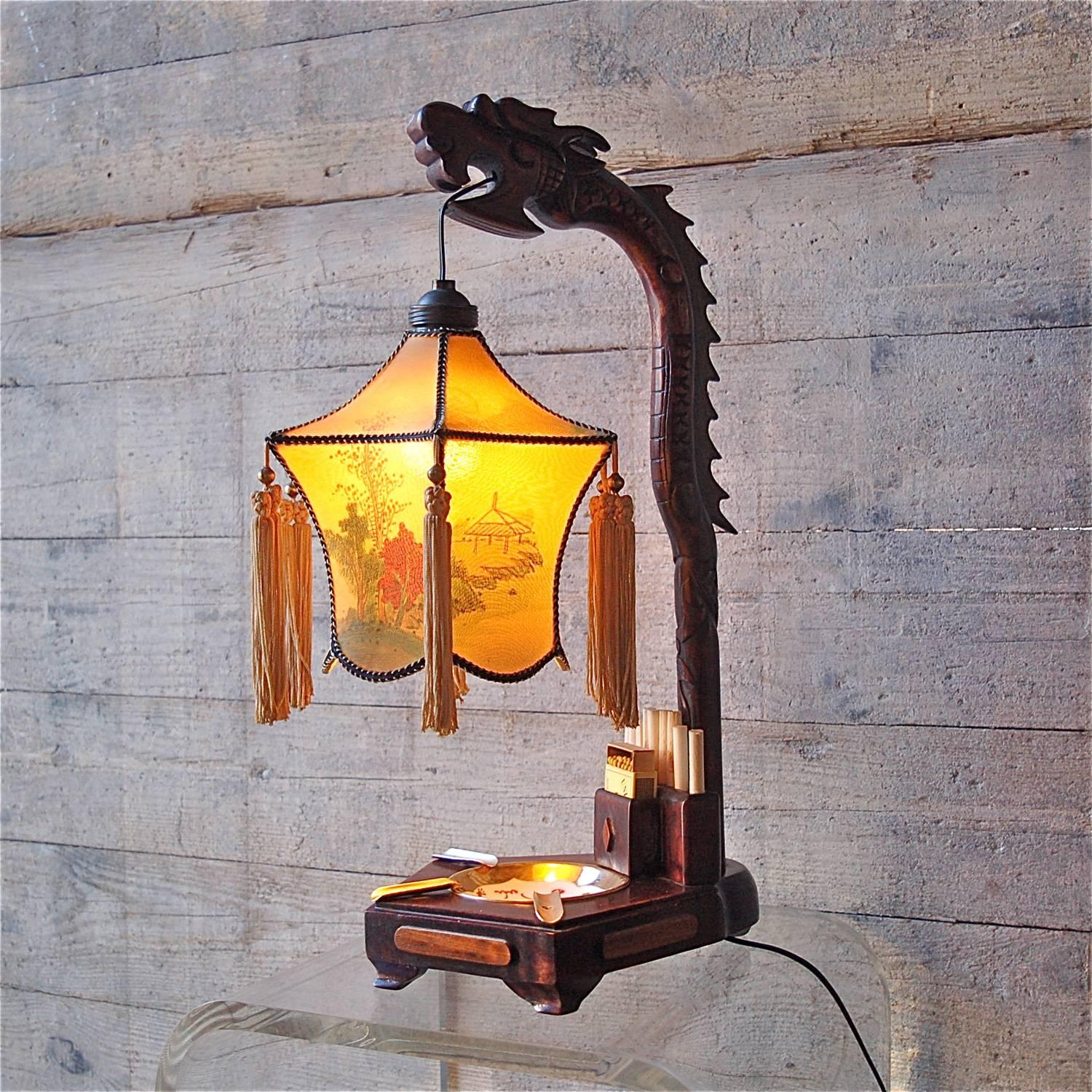 Chinese Dragon table lamp with ashtray and cigarette holder in original condition. The carved wooden dragon acts as a support or lamp base for a six facetted pagoda style shade with silk printed design depicting a Chinese coastal landscape with