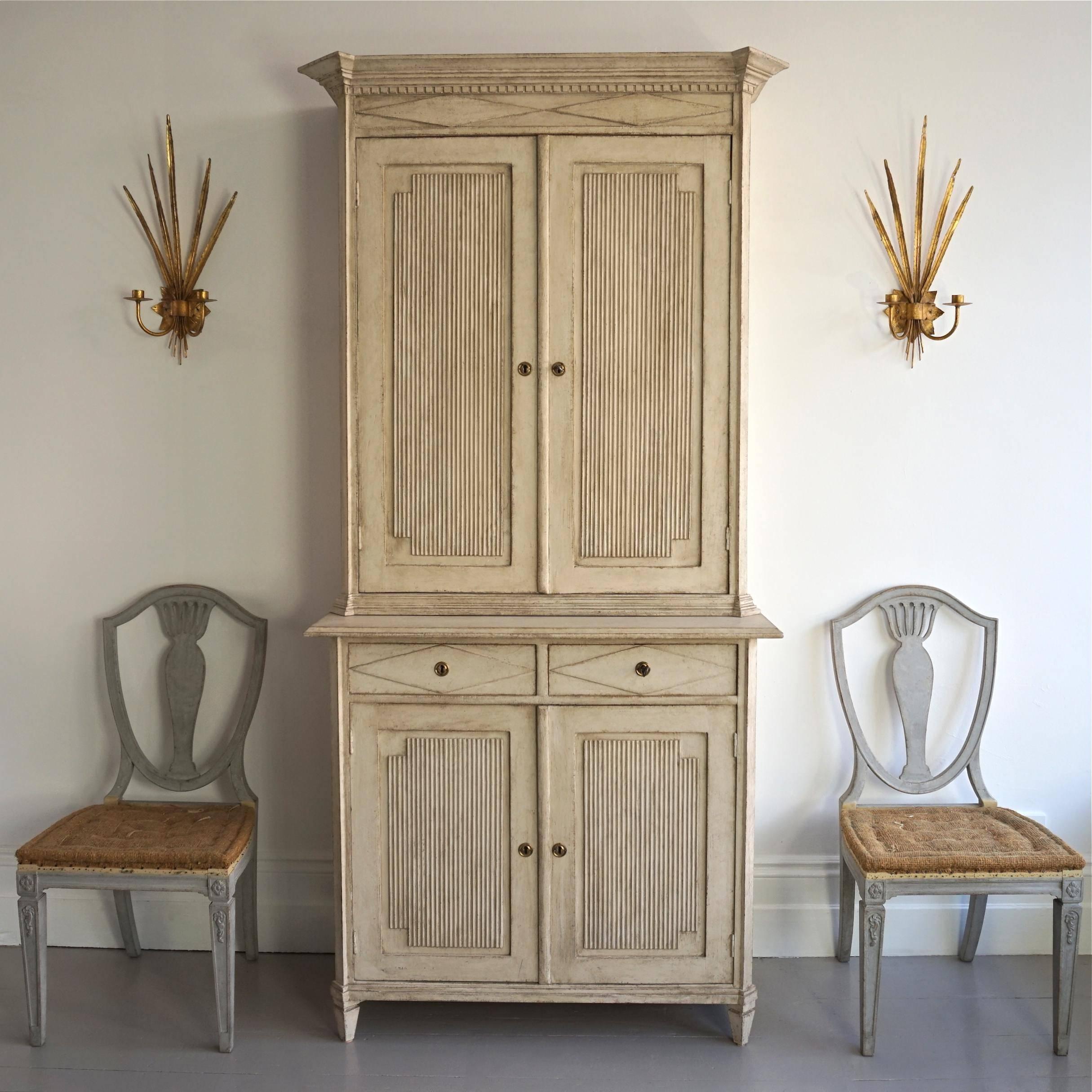 A very fine and richly carved 19th century Gustavian style cabinet featuring a beautiful overhanging pediment cornice with canted corners, dentil trim and diamond details, decorative panelled cupboard doors with vertical reeding, two drawers with