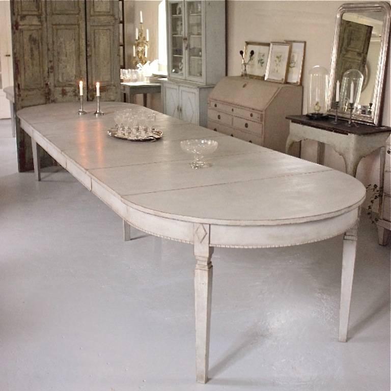 An exceptional, grand scale antique Swedish Gustavian style dining table that extends to over 14 feet in length with all five leaves inserted. This beautiful table features a decoratively carved apron and stands on elegant square tapered legs with