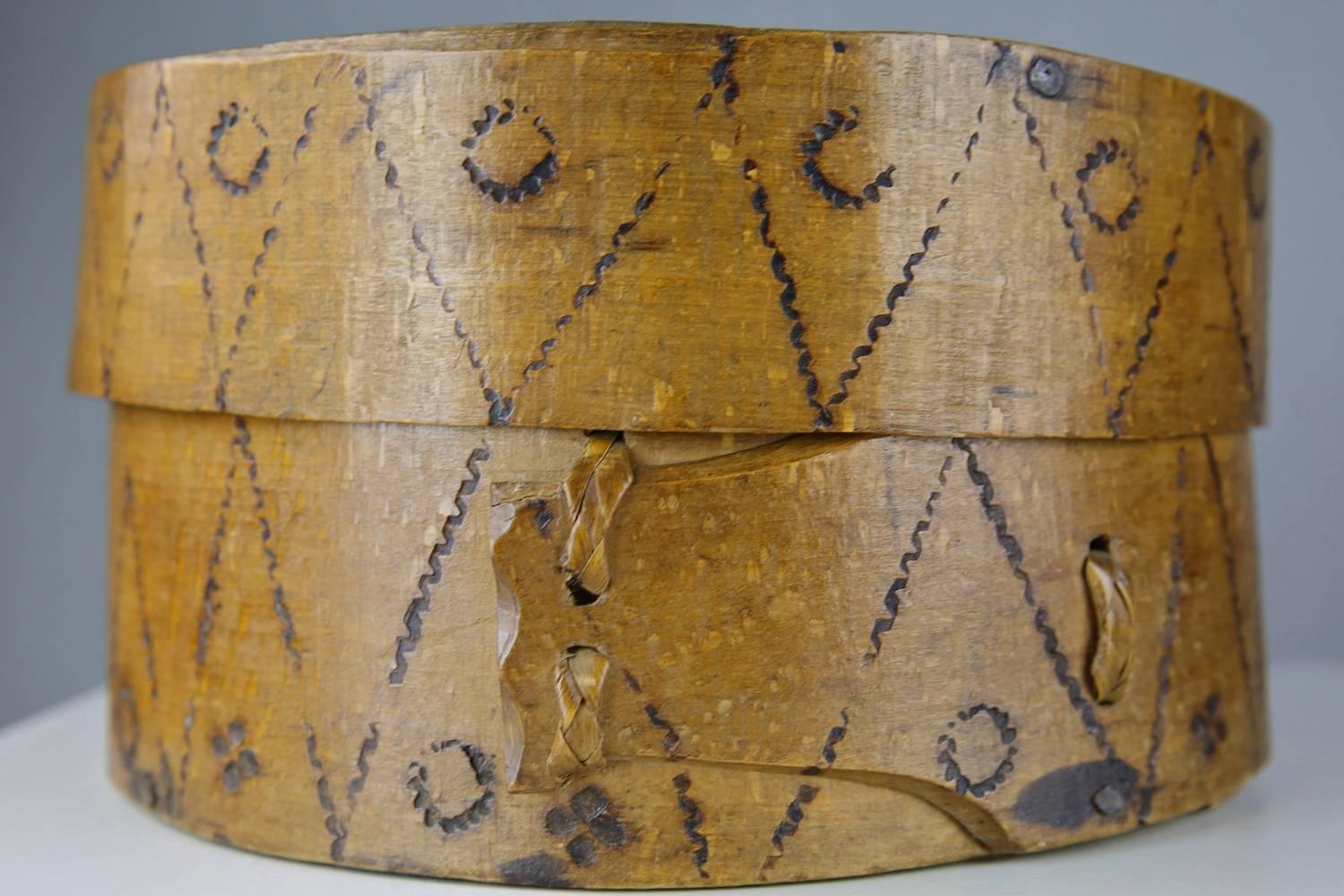 Box clever: handcrafted primitive bentwood box decorated with geometric poker work designs. With wonderful patina, and a pleasing tactile and unaffected quality, this receptacle is of banded construction with tree root ties holding its tongues in