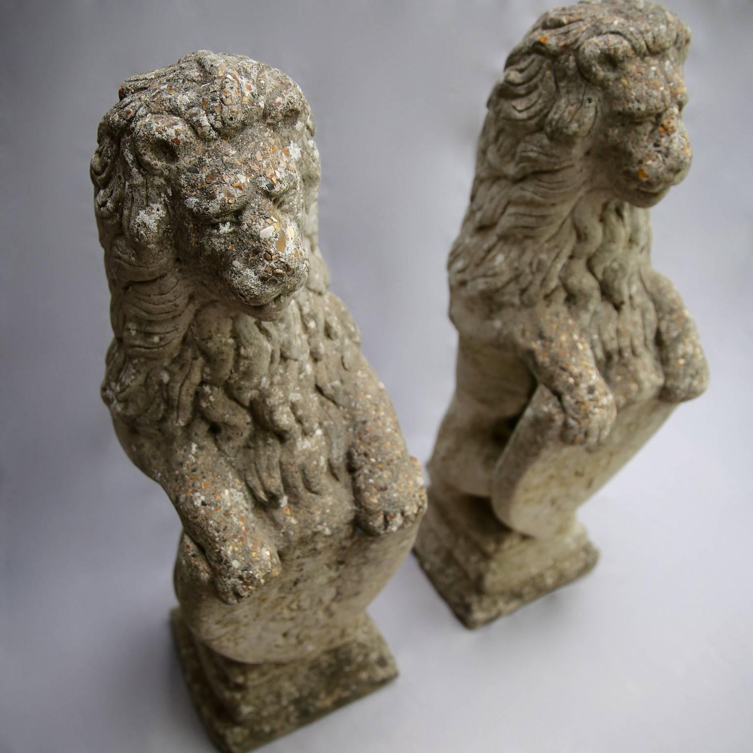 Lionheart: Imposing, tall pair of composite lion statues. Each holding a shield featuring a coronet over a further lion rampant, this duo are pleasingly weathered, and will only grow more so as they continue to age. With gently noble facial