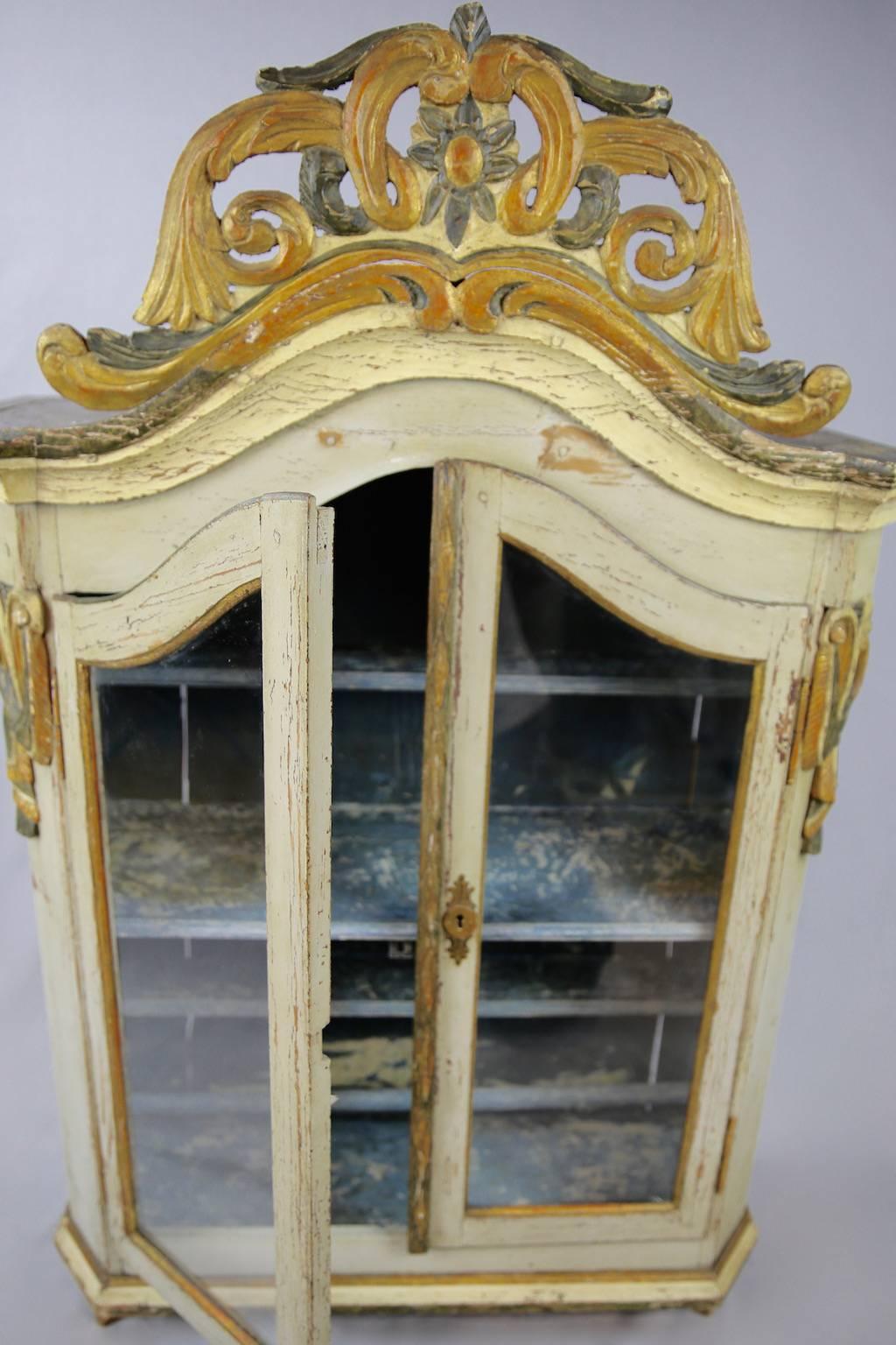 Rococo-nut! Beautiful little shelved Swedish cabinet dating from the late 1700s. Featuring an elaborately carved crest in an old-gold and faded black colourway above a domed, off-white and pale grey case with carved swags to either side, this piece