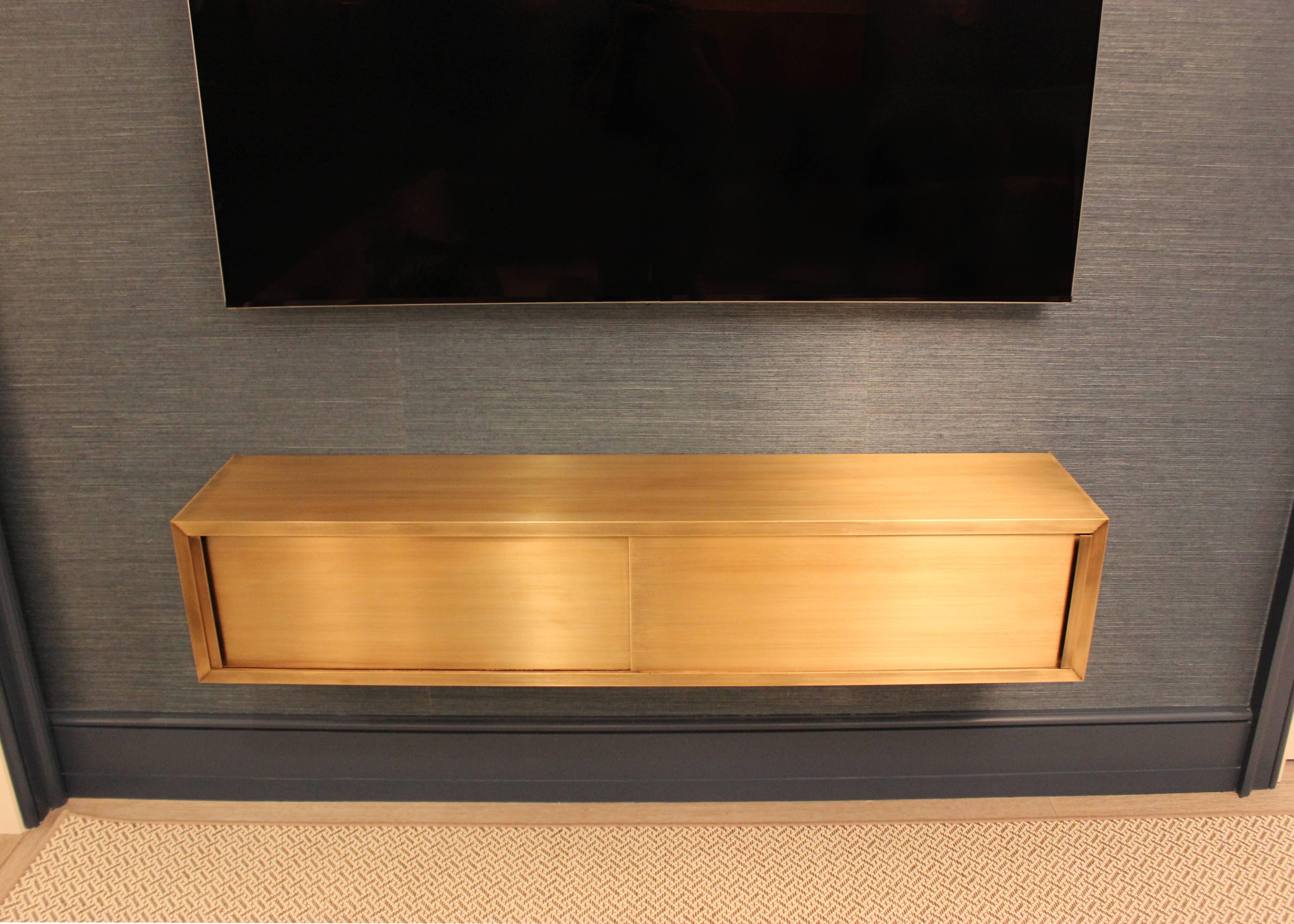 Wall-mounted console in bright satin patinated bronze finish. Stained walnut interior houses media equipment. Available in custom sizes, finishes and materials.