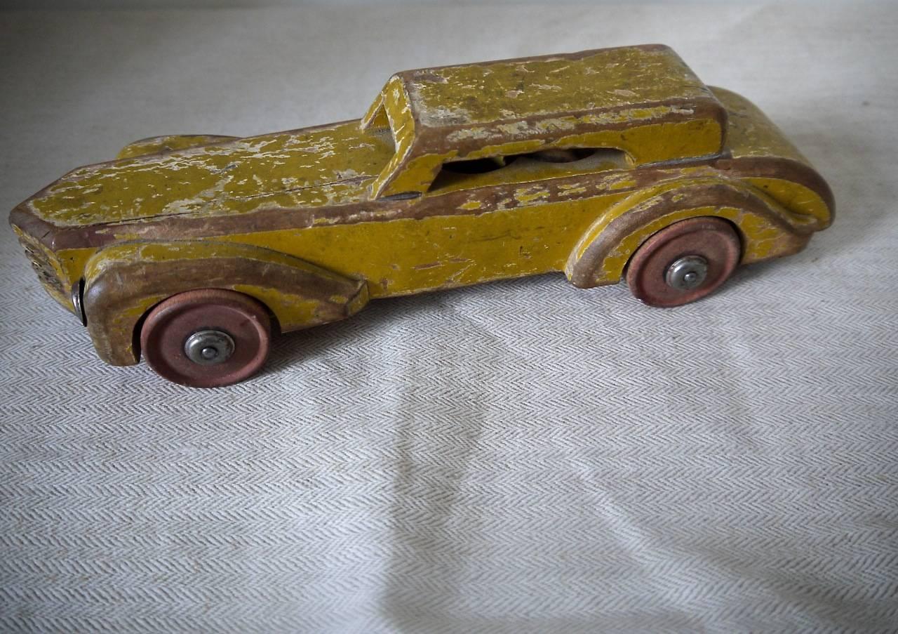 French painted wood toy car, circa 1930s. The car has a very elegant shape and is painted a warm saffron yellow. Was a much loved and played with toy.