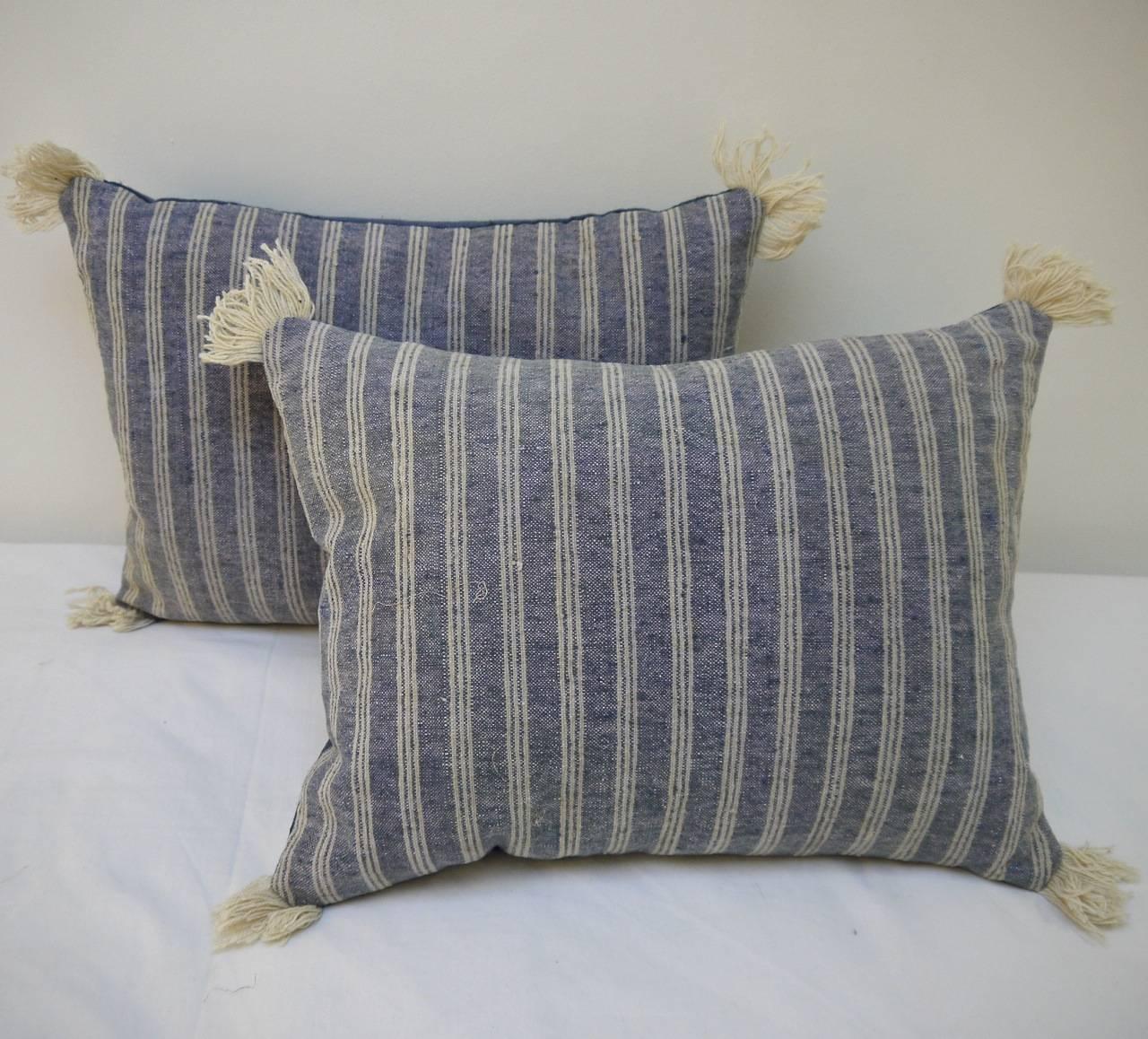 A French 19th century woven cotton and wool cushion with antique wool fringing on each corner. The soft indigo stripe alternates with a wool stripe of a very pale greenish blue hue. Backed with a dyed 19th century French linen and slipstitched
