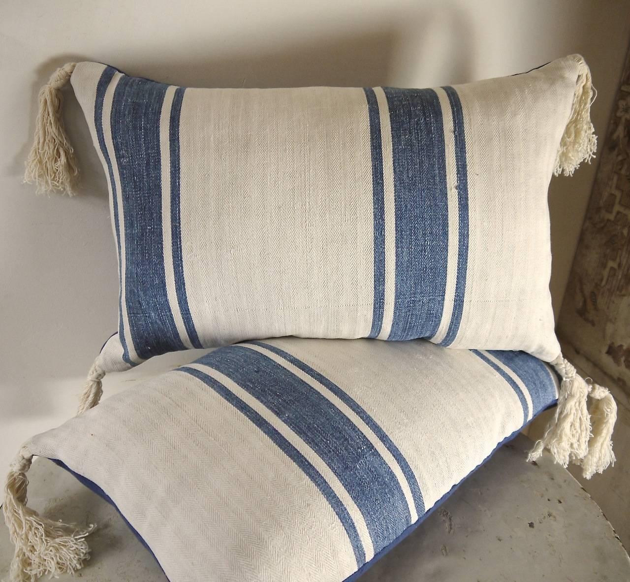 Pair of late 19th century French linen herringbone cushions with indigo stripes. The linen is softly worn and washed with age with a faded indigo stripe and a charming patch. Has a great look and feel. Antique French cotton tassels on each corner.