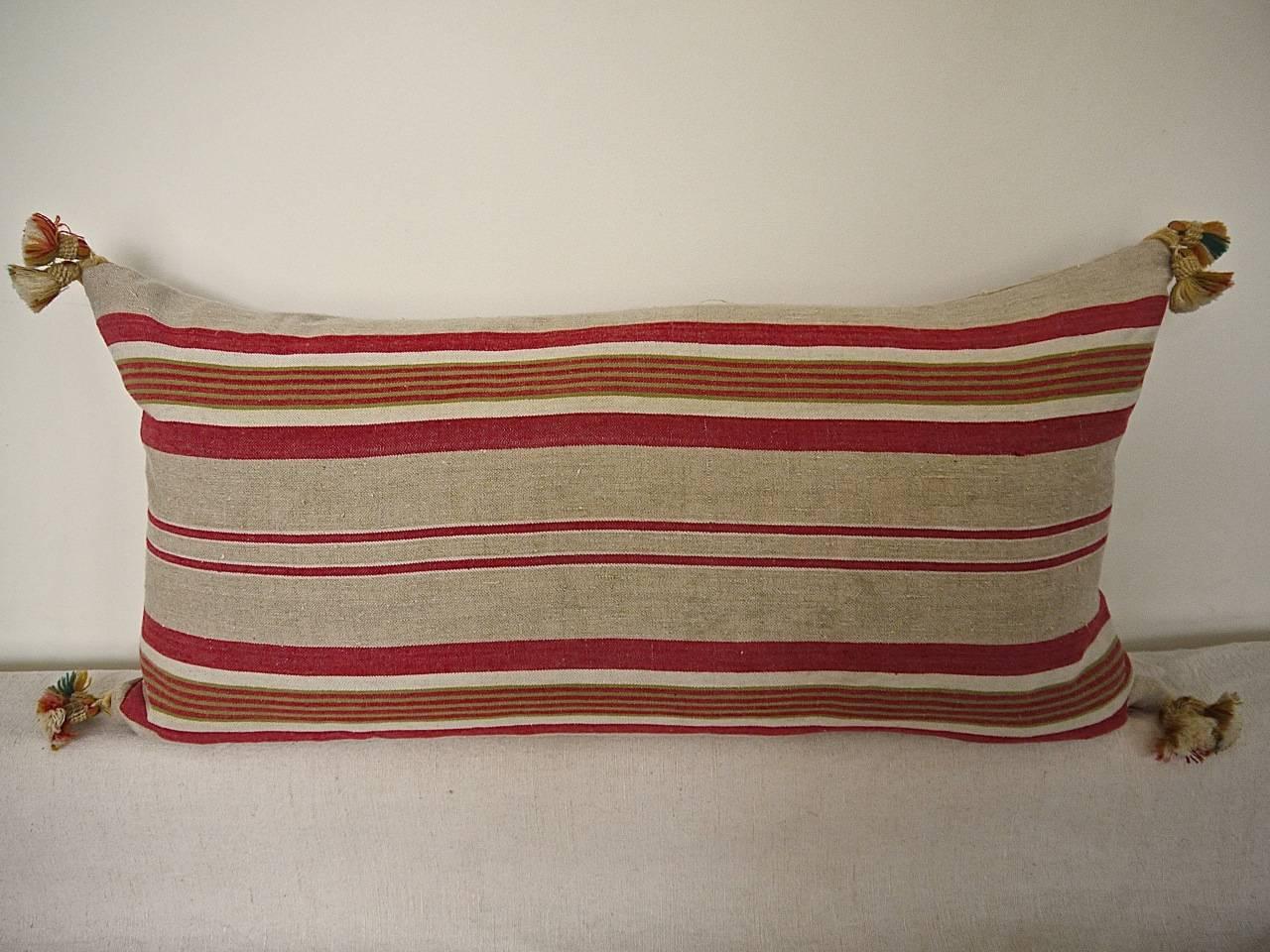French linen ticking cushion in stripes of red, beige and thin khaki green. With 19th century, French wool tassels on each corner. Slip-stitched closed with a duck feather insert.