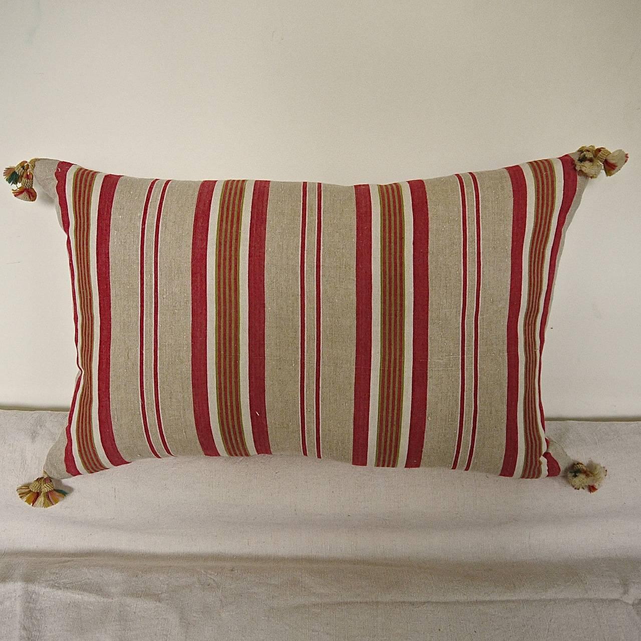 French linen ticking cushion in stripes of red, beige and a thin khaki green. With 19th century French wool tassels on each corner. Slips-stitched closed with a duck feather insert.