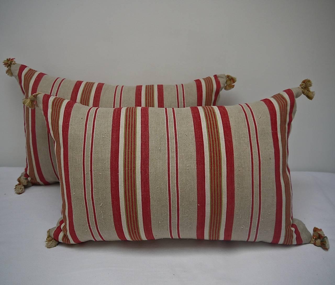 Pair of French early 20th century linen ticking cushion in stripes of red, beige and khaki green. With 19th century French wool tassels on each corner. Slip-stitched closed with a duck feather insert.