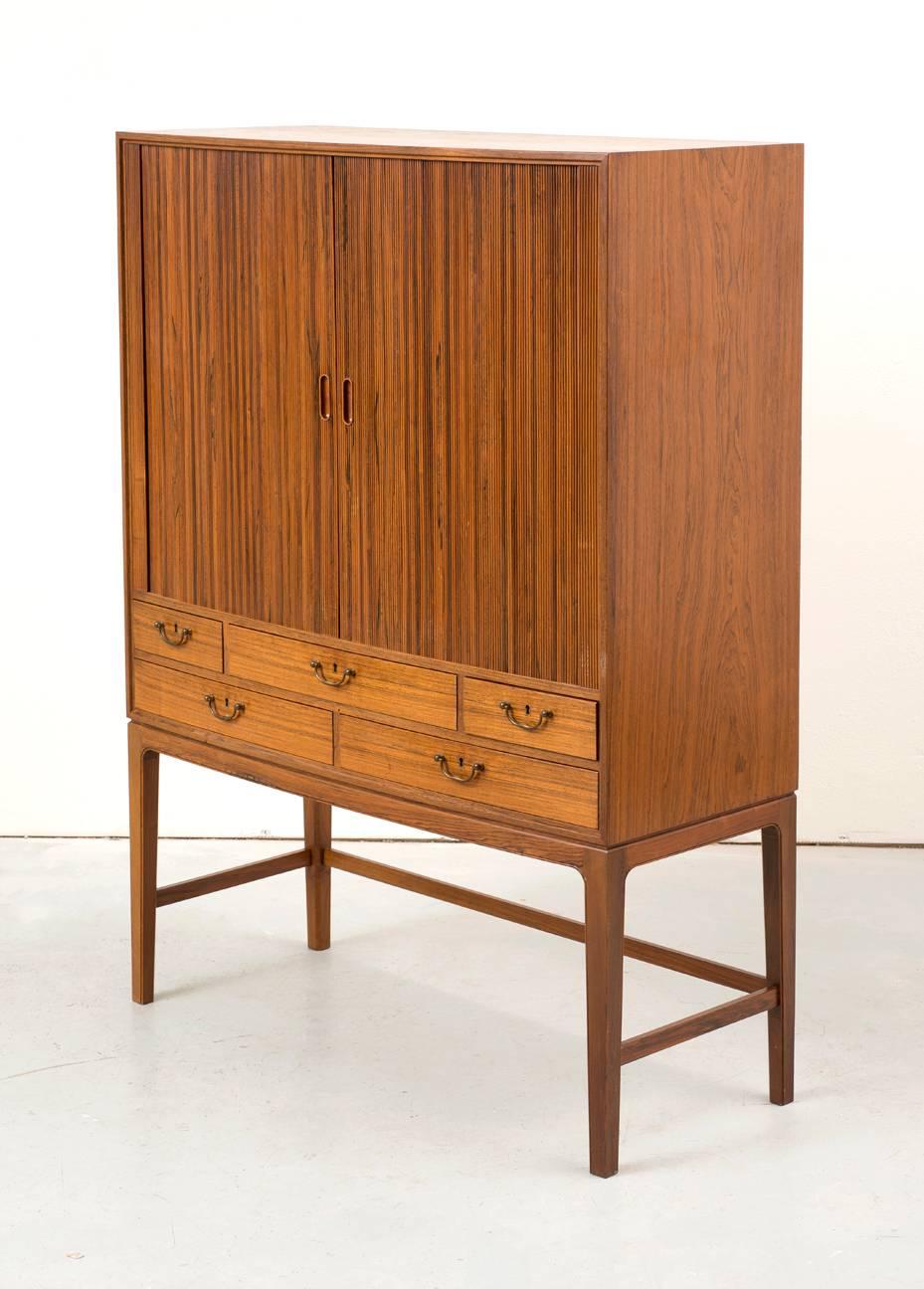 Tall cabinet of Brazilian rosewood. Slightly curved front with tambour doors and five drawers with original brass pulls. Made for Illums Bolighus, circa 1960s.