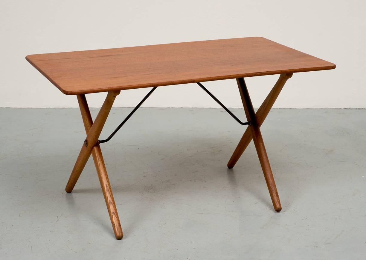 A Classic cross-legged table by Hans Wegner for Andreas Tuck. Tabletop in teak and frame in oak with brass stretchers.