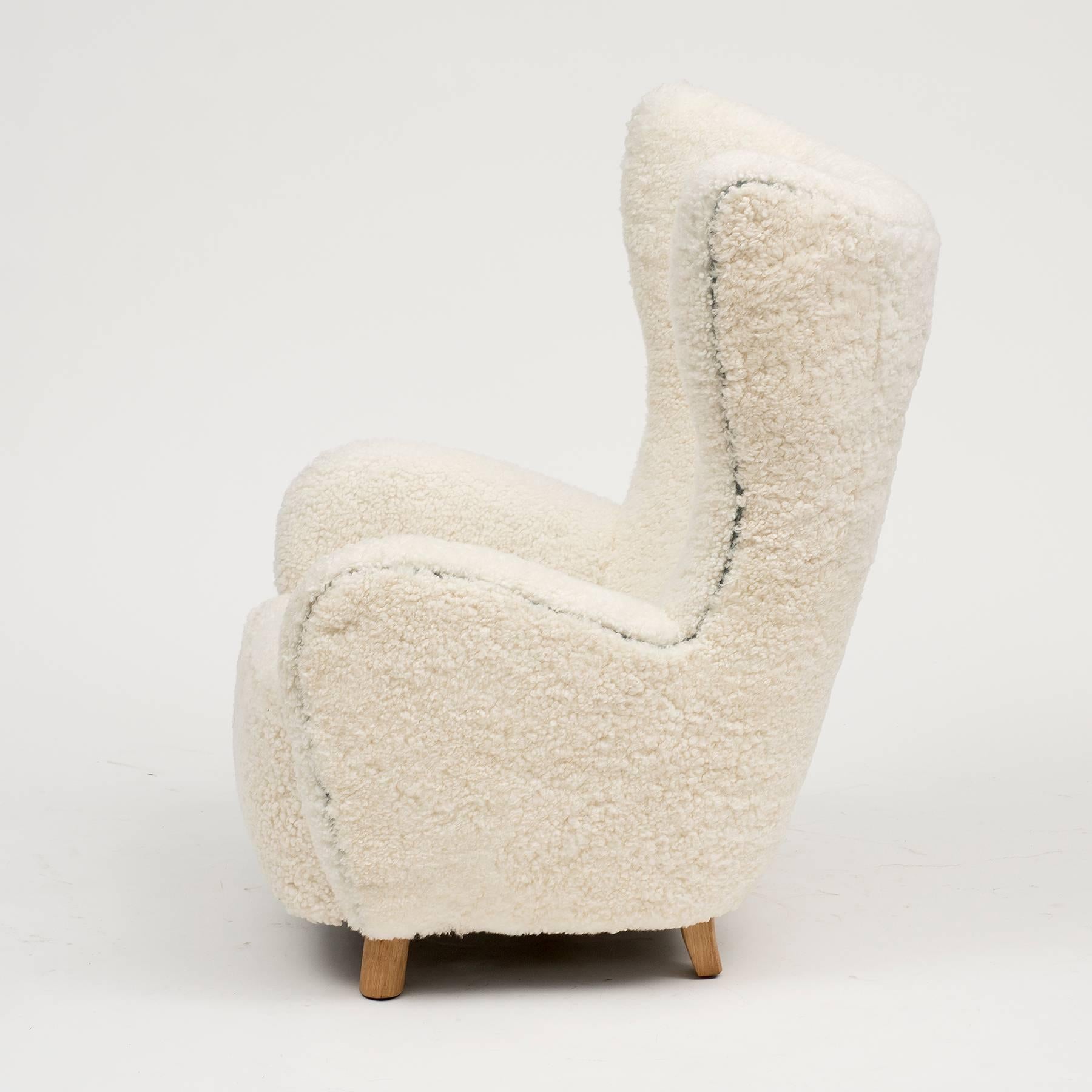 A wingback chair by Mogens Lassen in white sheepskin with grey/blue suede piping and buttons, and oak feet, Denmark, 1930s.