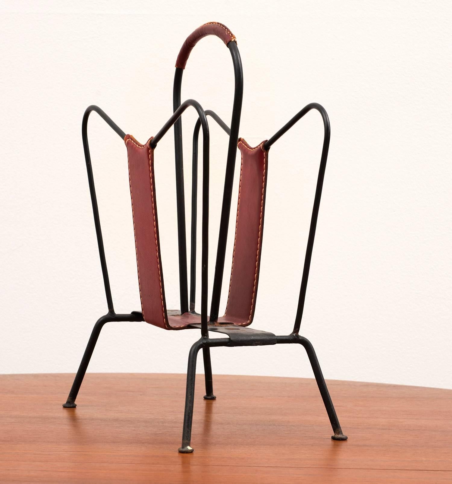 Classic magazine rack by Jacques Adnet in aged iron and red leather with contrast stitching, France, 1950s.