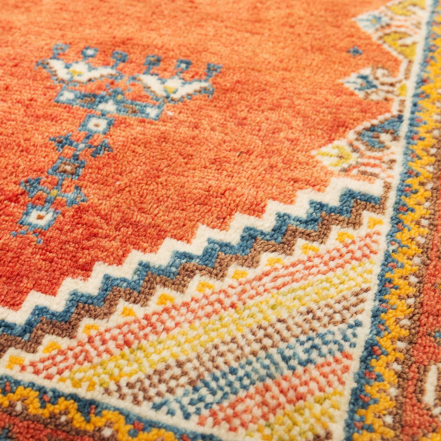 A handwoven wool Moroccan tribal rug from the 1950s in orange background with blue, cream and yellow accents. In excellent condition.