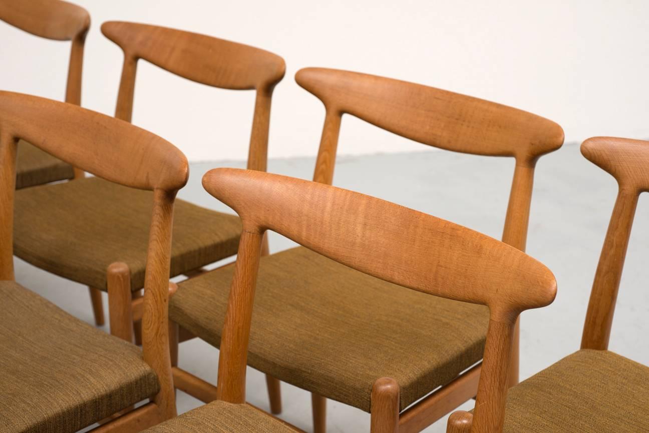 A set of eight original W2 dining chairs in teak and original variegated khaki wool upholstery by Hans Wegner, circa 1953.