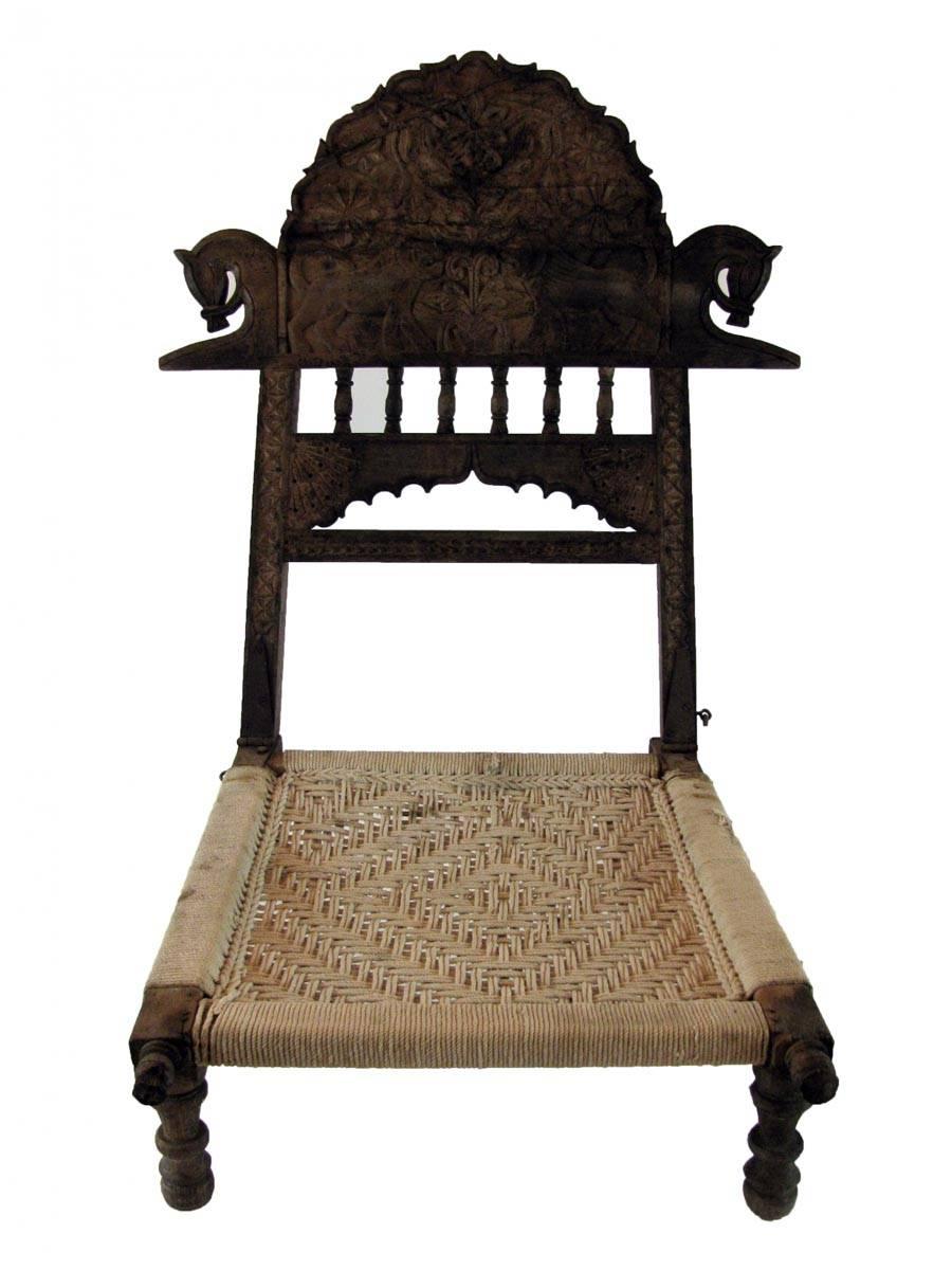 A rare Indian folding Pida chair featuring hand-carved horses, lions, flowers and geometrical patterns to the front and back of the shaped backrest, a tribal hand-carved from solid teak decoration  with its original patination.  
The chair features