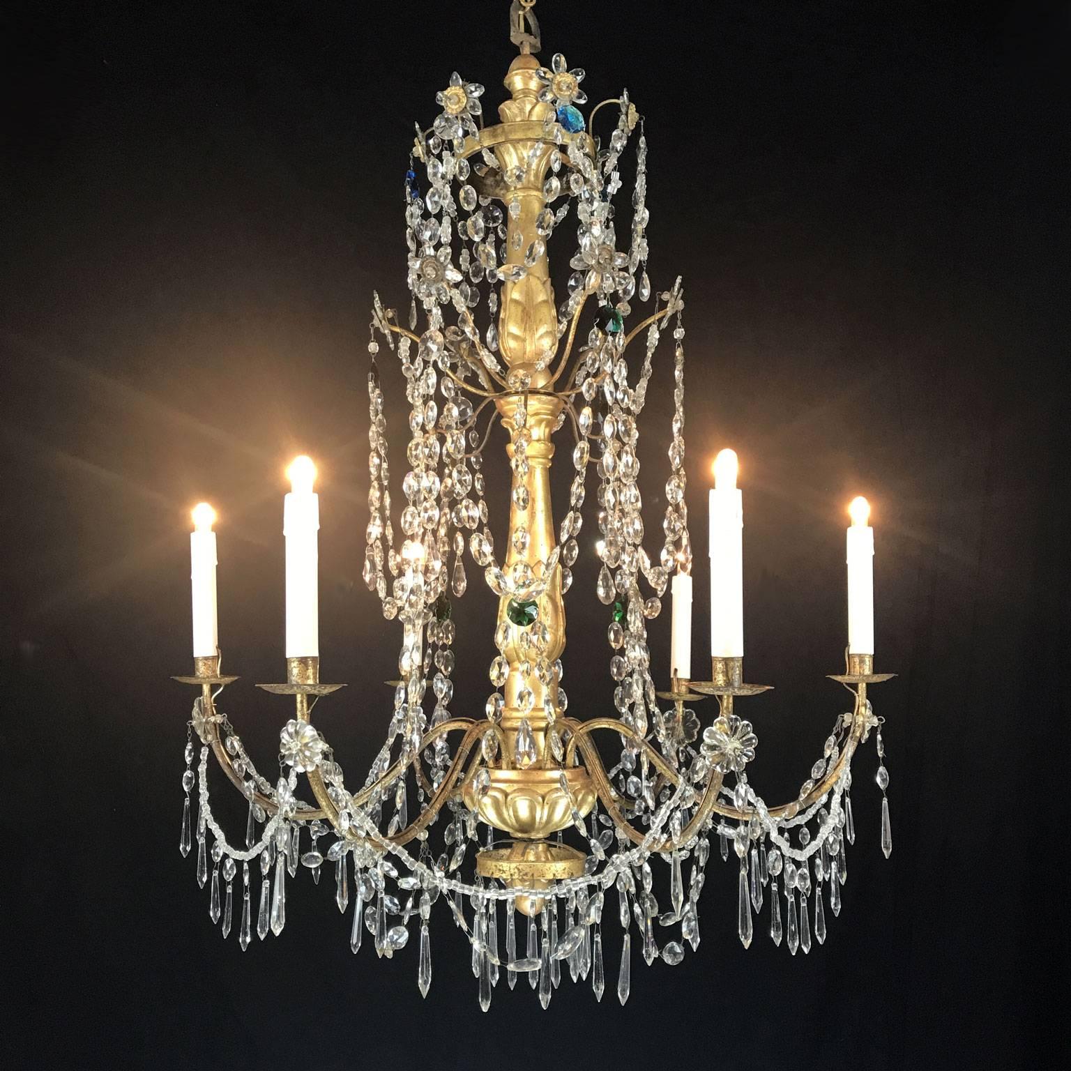 Late 18th century Genoese Empire crystal chandelier with a giltwood carved stem, featuring six curved candle arms draped with cut crystal beads and pendants and is decorated with a few blue and green crystals and original gilded and repoussé brass