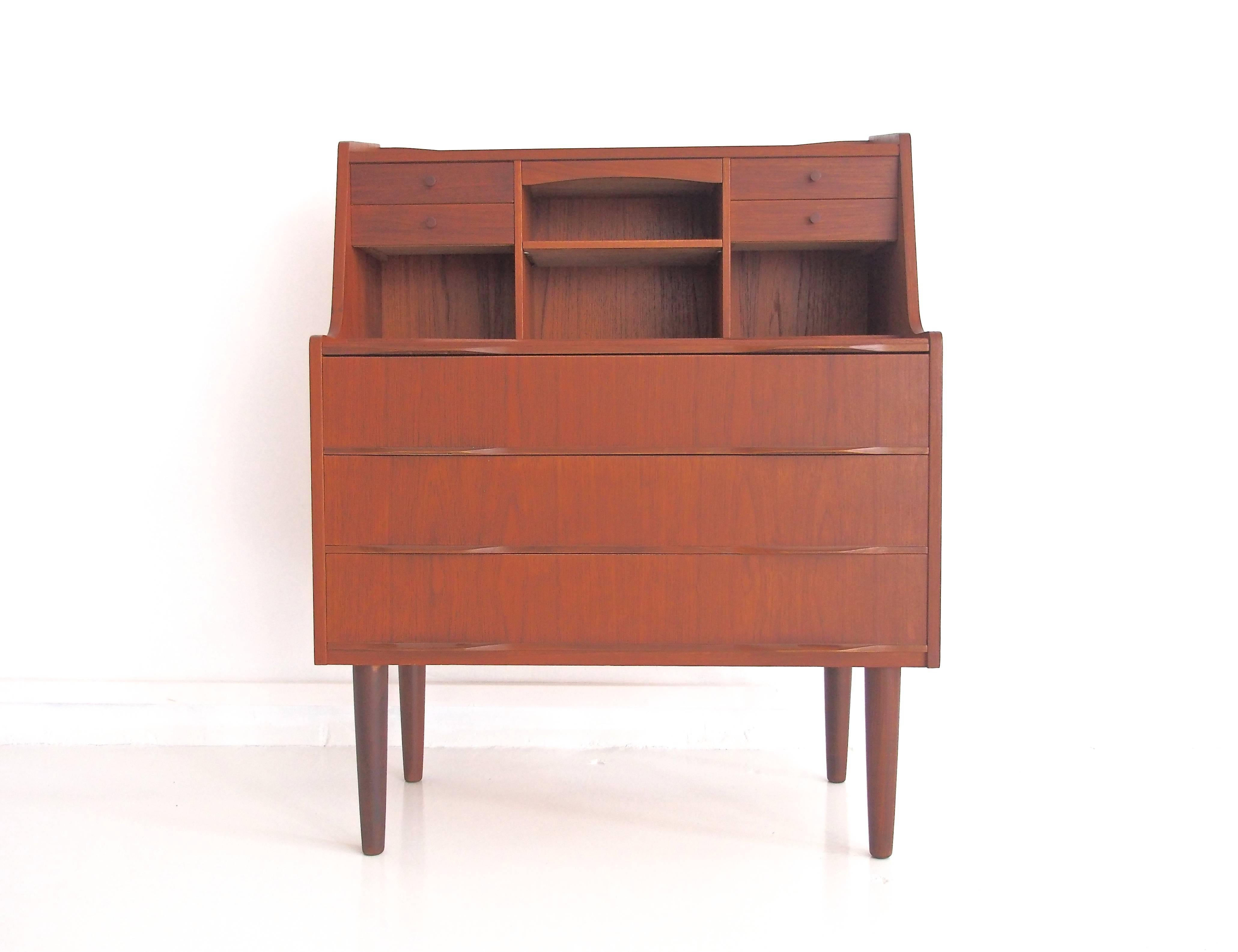 Bureau or dressing table made of veneered teak on round tapered legs. Front with three large drawers. On the top, four small drawers and compartments, as well as a pull-up mirror and a pull-out writing board. Recently restored.