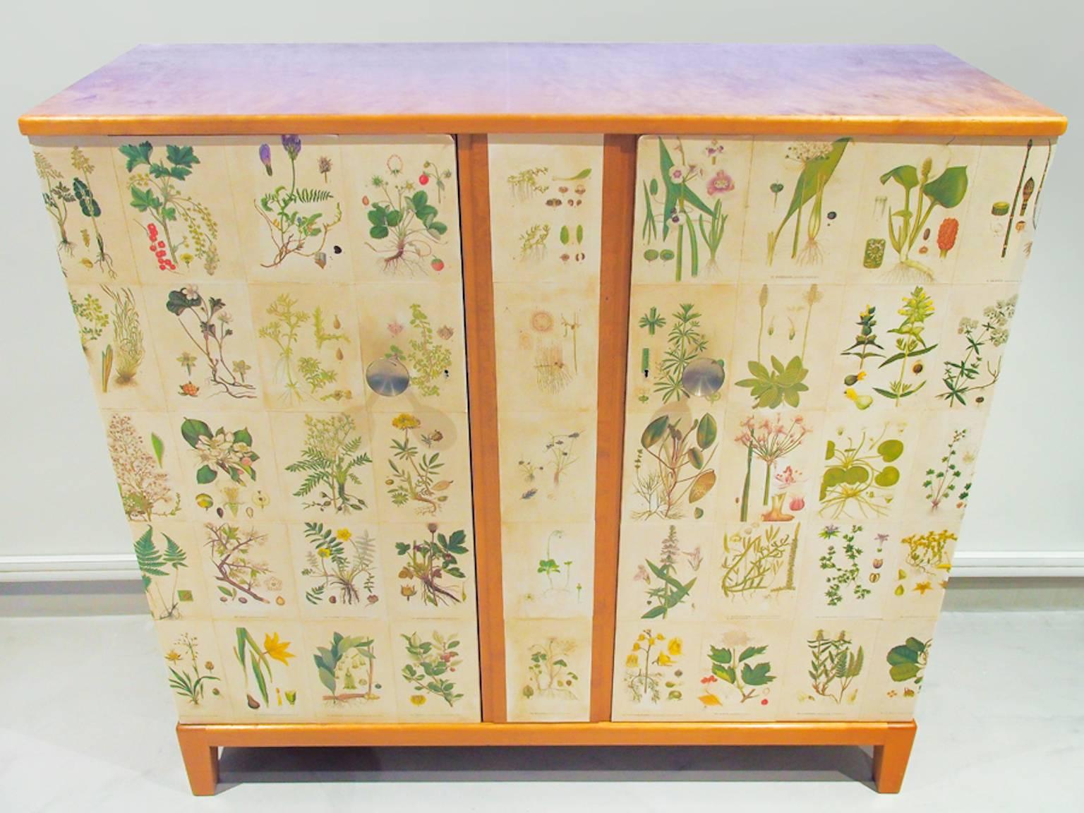 1960s birch cabinet decorated with printed paper. The flower illustrations are from the book "Nordens Flora" by Swedish botanist and botanical artist Carl Axel Magnus Lindman (1856-1928). Front with two doors enclosing two drawers and