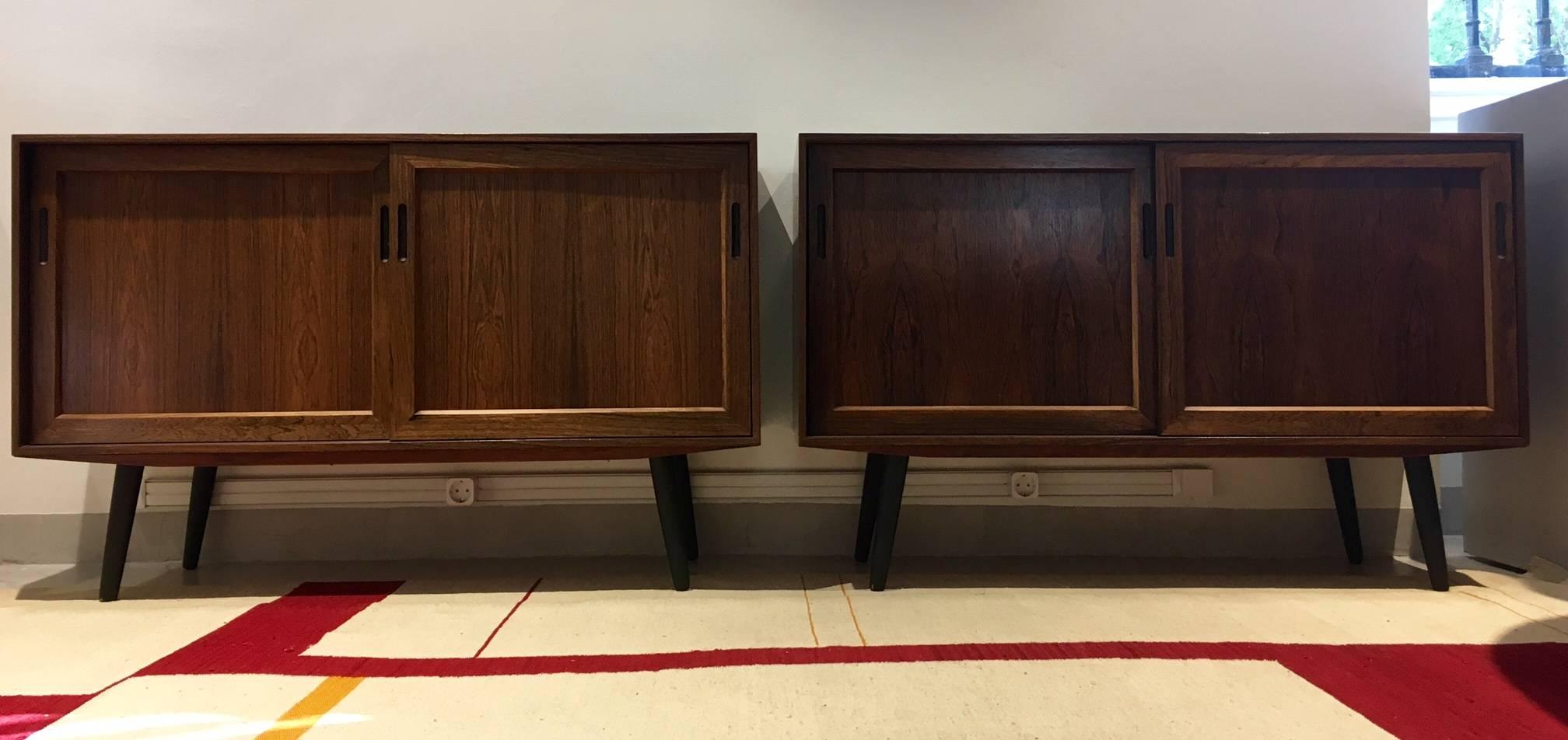 Pair of midcentury sideboards made of Rio rosewood by unidentified Danish furniture producer. Each has two sliding doors and interior fitted with shelves. Round stained wood legs. Excellent condition.
