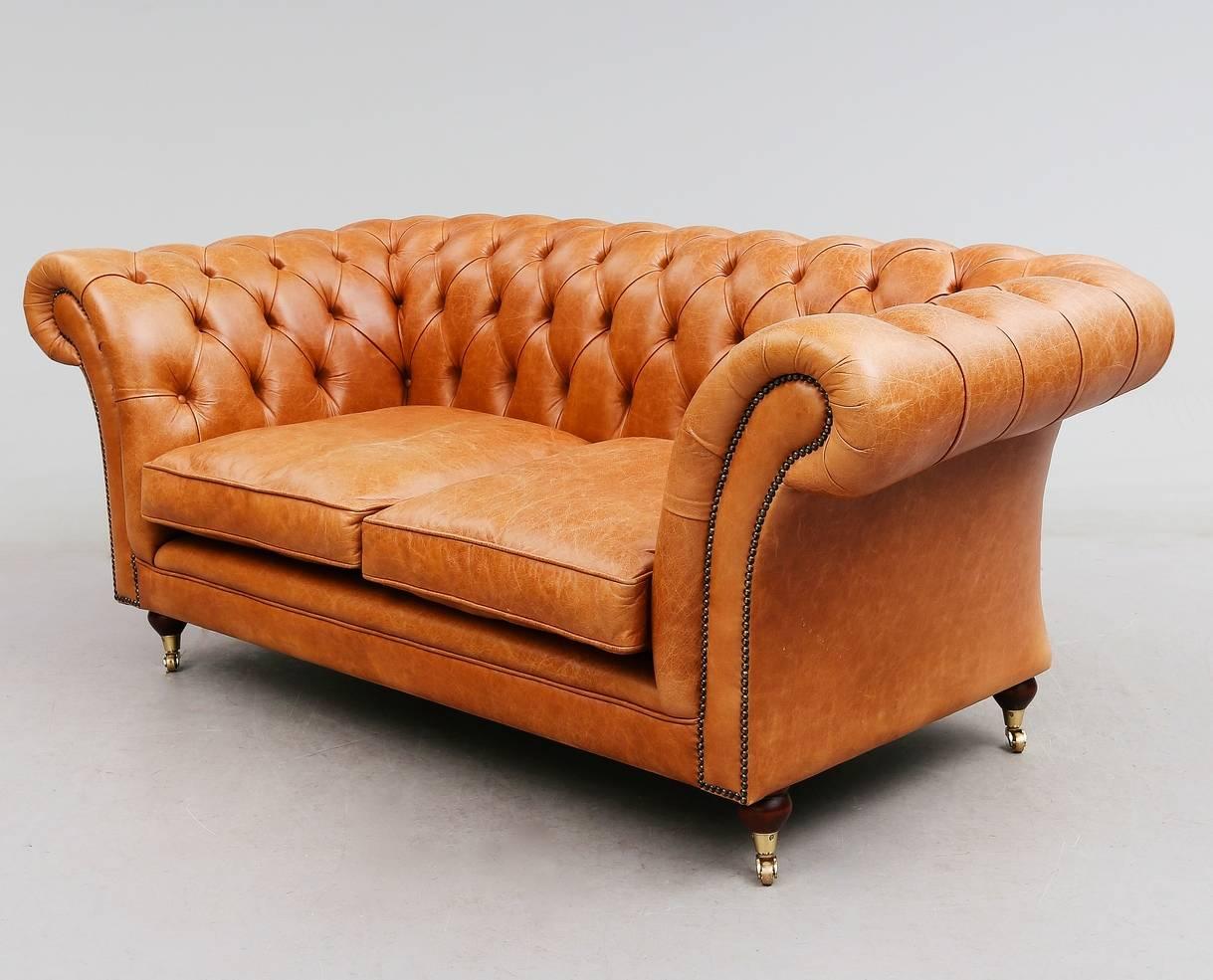 Classic Chesterfield style sofa tufted with light brown leather. Rolled arms and back, two loose seat cushions. Stud decorations.