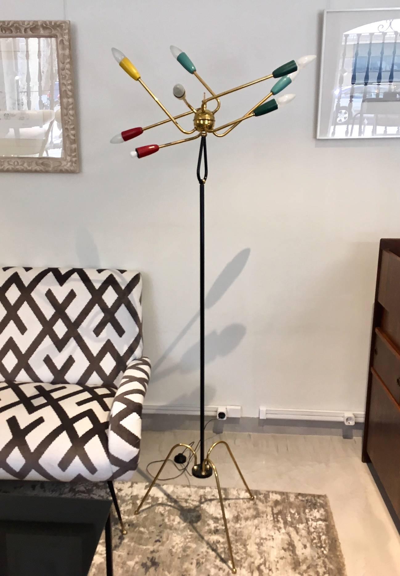 Italian floor lamp, in the style of Stilnovo. Rod varnished in black, three bent brass feet, the shaft ending in a loop with sphere at the top, from which emanating eight L-shaped bent branches of lights with sockets varnished in color. Sphere and