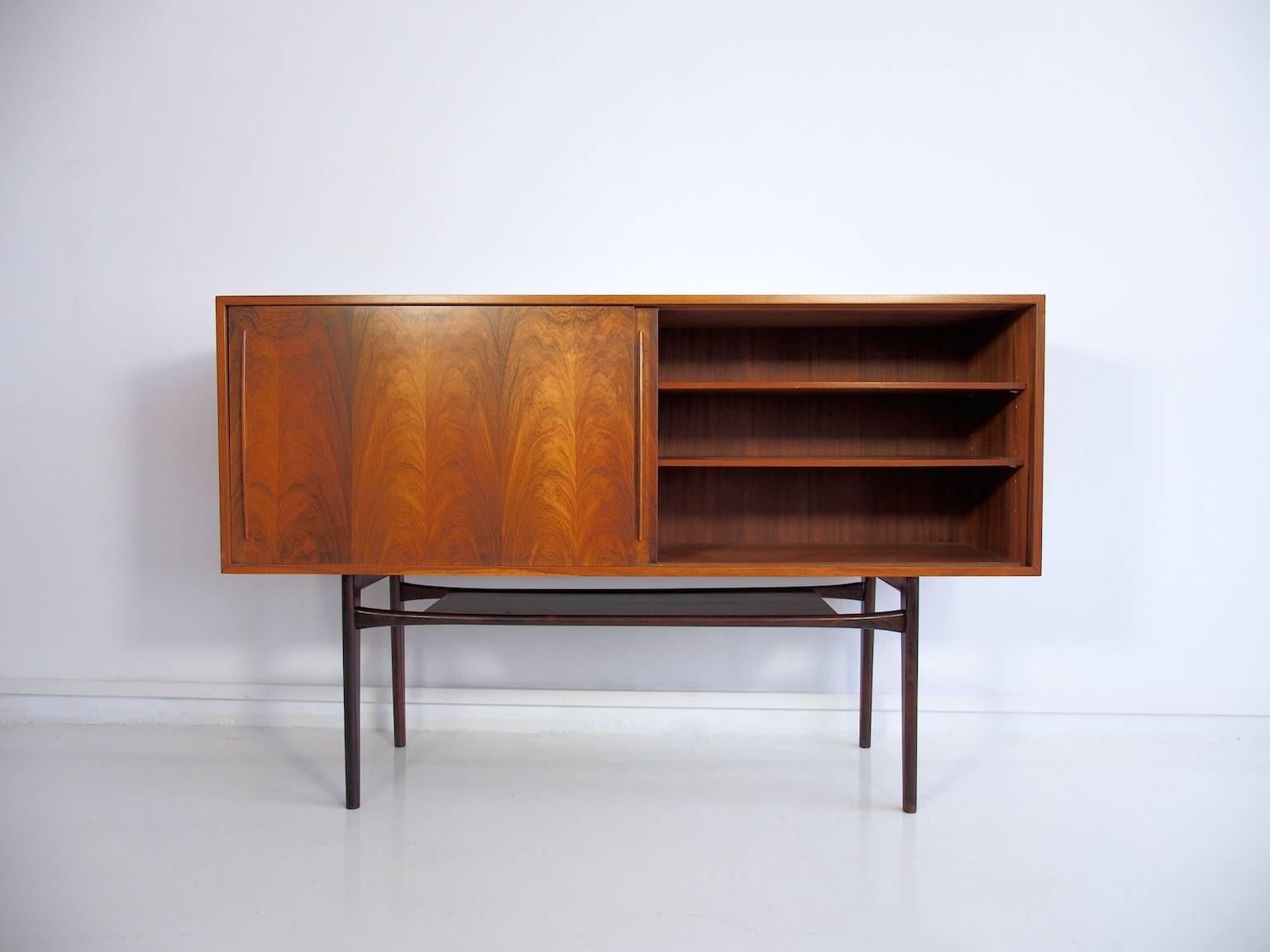 Tall rosewood sideboard with two sliding doors, behind which are shelves and pull-out trays with green felt lining. Mounted on unoriginal base. Recently restored.