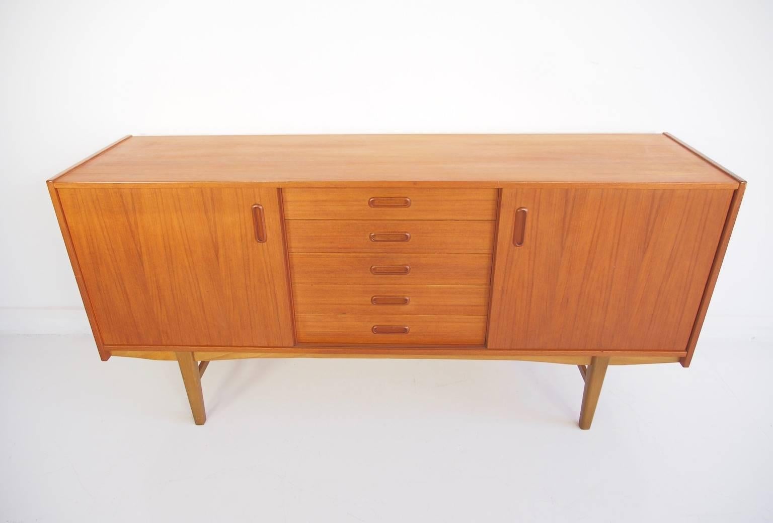 Teak sideboard with five drawers with green lining and doors on both sides, behind which are shelves. Partially restored. Minor dents on the side and the corner of the sideboard, pictured.
