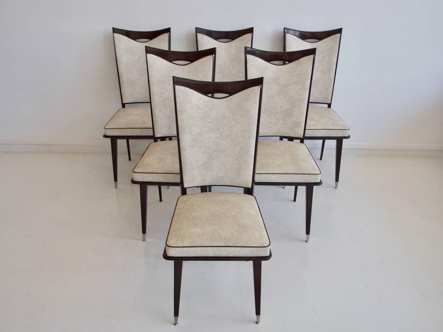 Six French style dining chairs on dark lacquered oak, circa 1960. The seat is covered with cream-colored and grey marbled synthetic leather with tobacco-brown piping, chromium-plated metal caps at the bottom of the legs.