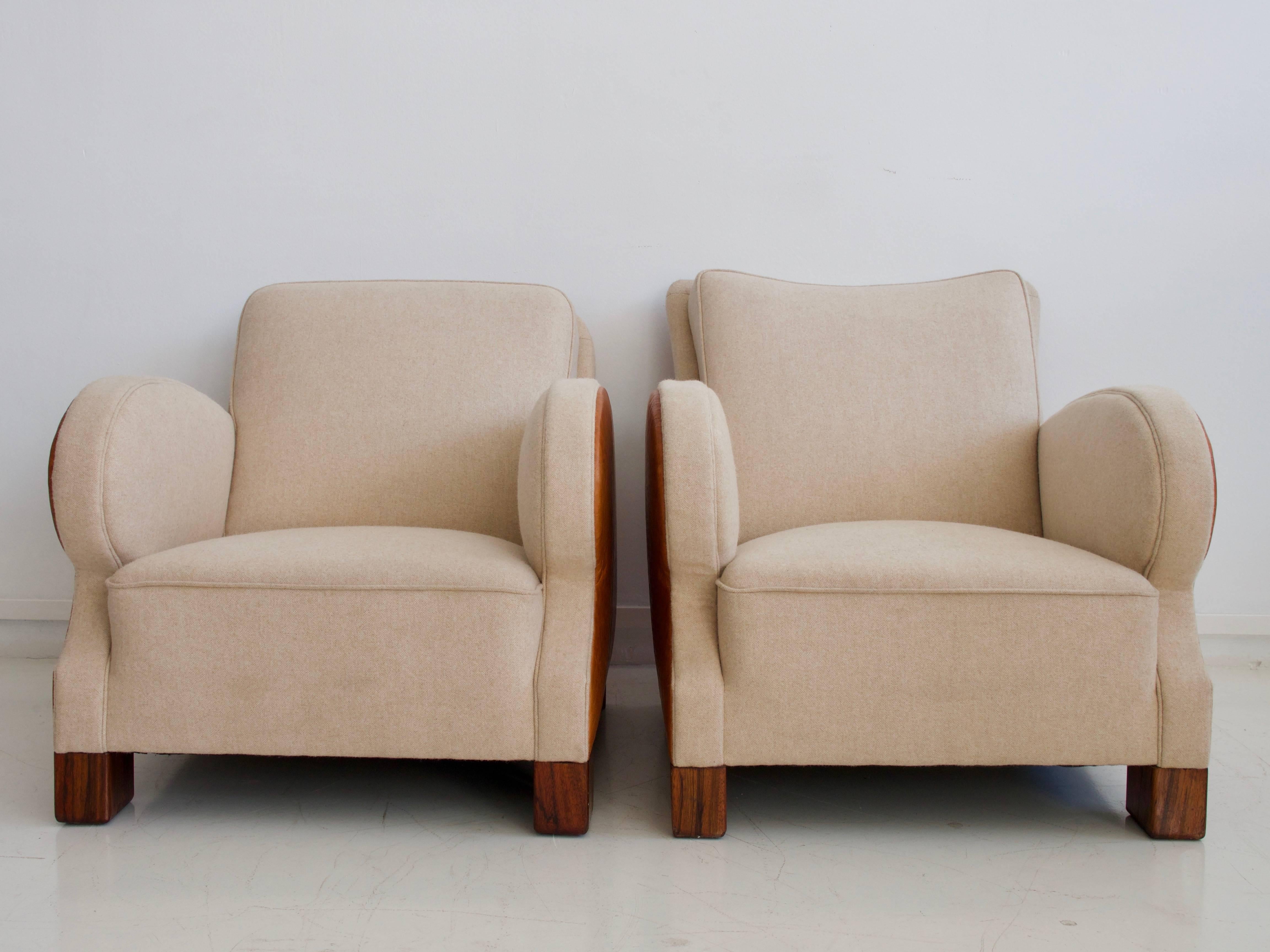 Two Art Deco style armchairs from circa 1930s with intentionally slightly different backrests. These elegant lounge chairs are reupholstered in beige wool and cognac colored leather, legs in stained wood.