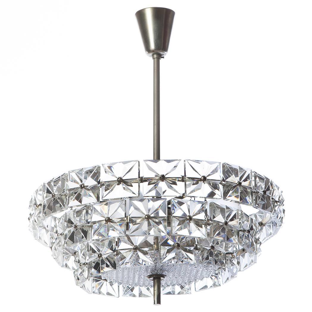 Majestic three-tier chandelier with square-shaped crystals with faceted-star ornaments hanging from a chrome frame.