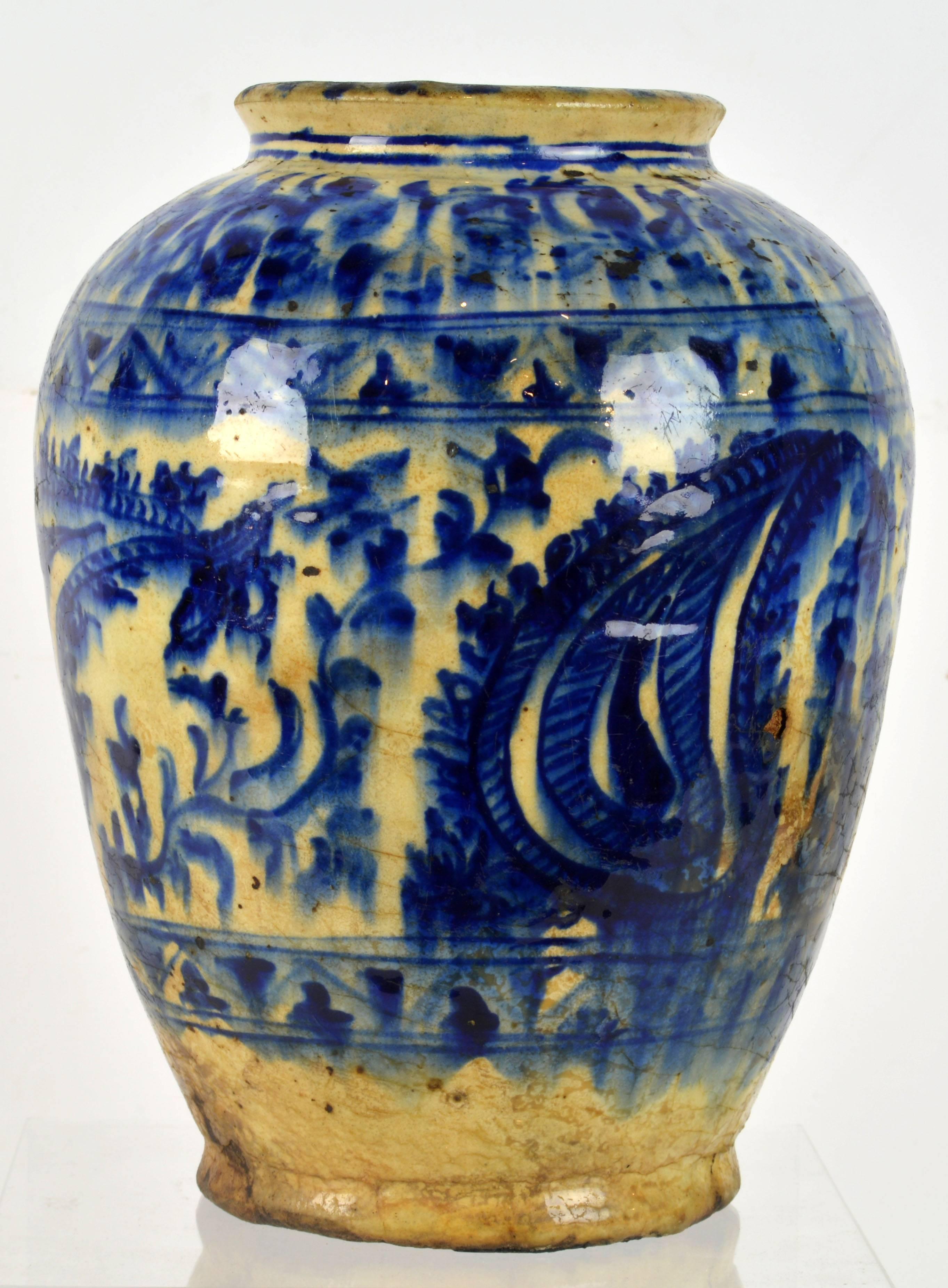 Standing 10.5 in. tall this Islamic museum quality pottery jar of great authenticity features a tapering baluster form decorated with blue and white glaze in a typical Syrio-Persian paisley style along with scrolling foliage and ornamental bands.
