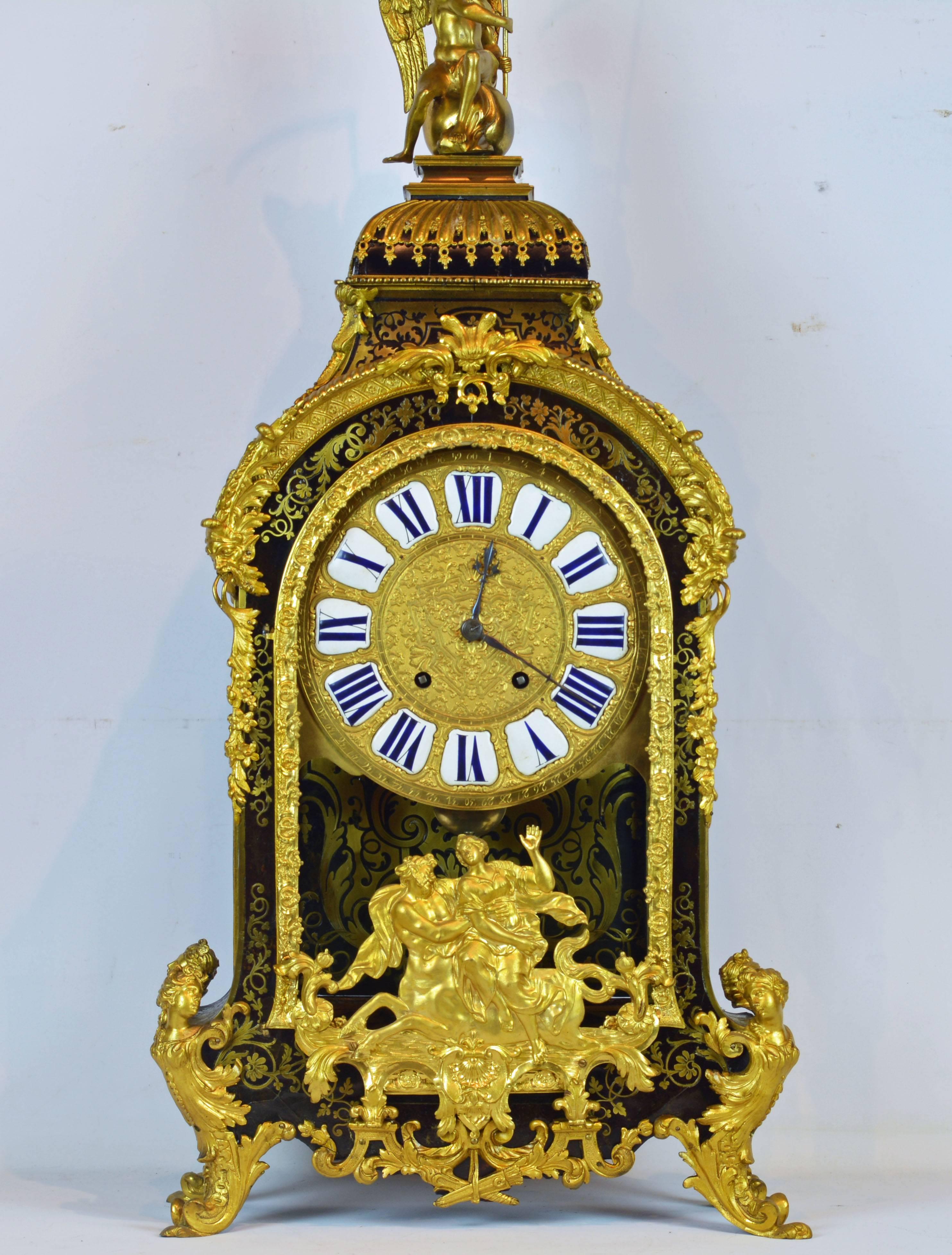Standing 43 inches tall this impressive clock features an arched pediment surmounted by a gilt bronze figure of the archangel St Michael seated on a globe and holding up his banner. The Boulle style brass inlaid case, richly edged by scrolled ormolu